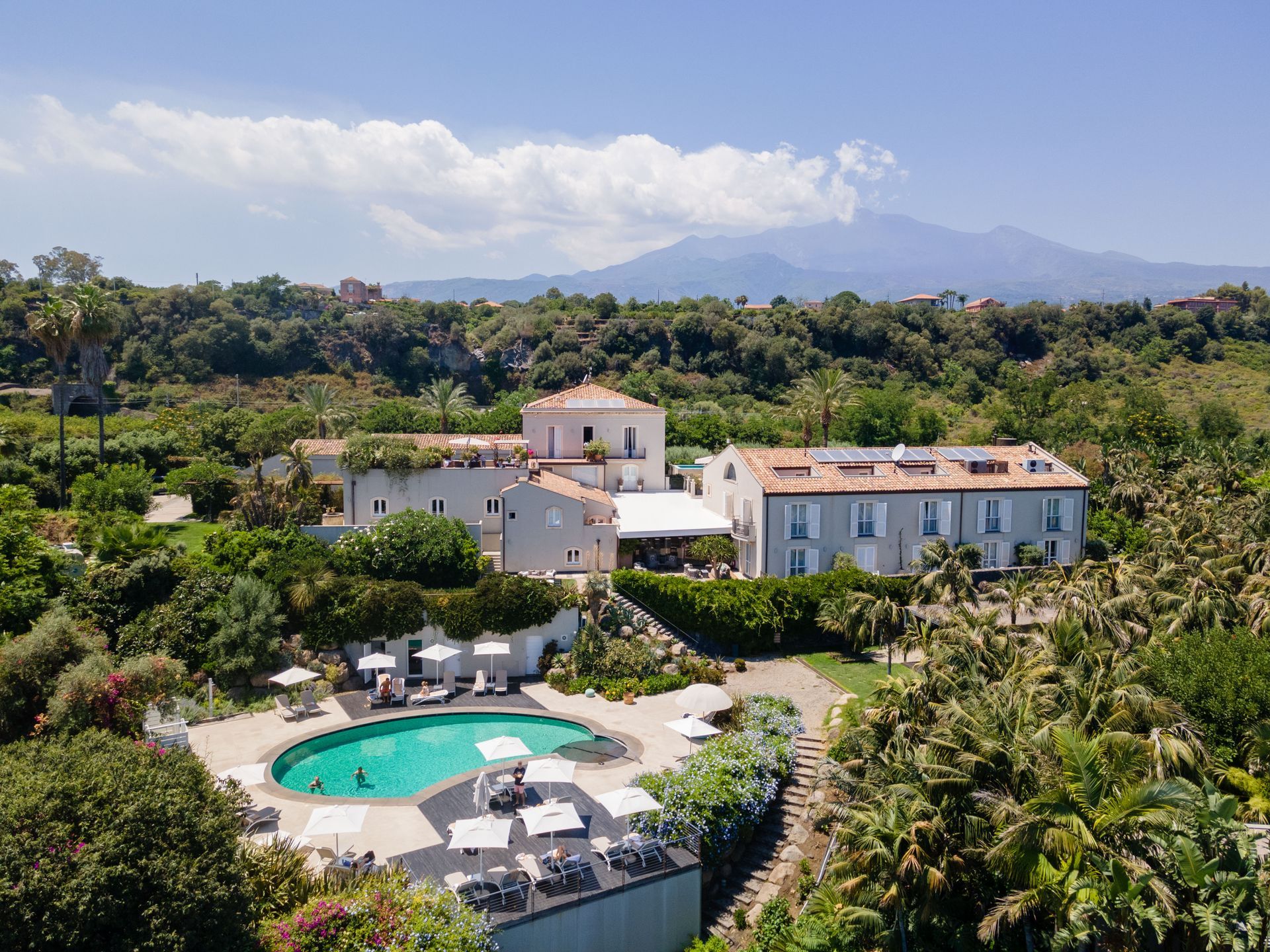 Hotel with pool surrounded by lush greenery. Mountain in the background. Sunny day.