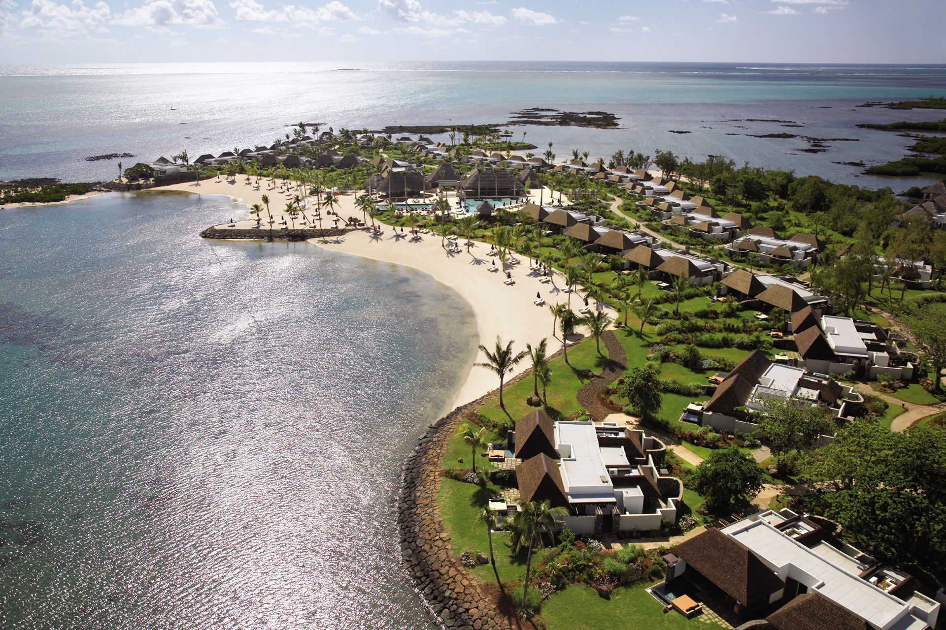 Aerial view of a Four Seasons at Anahita Mauritius  with villas, palm trees, and turquoise water across a curved shoreline