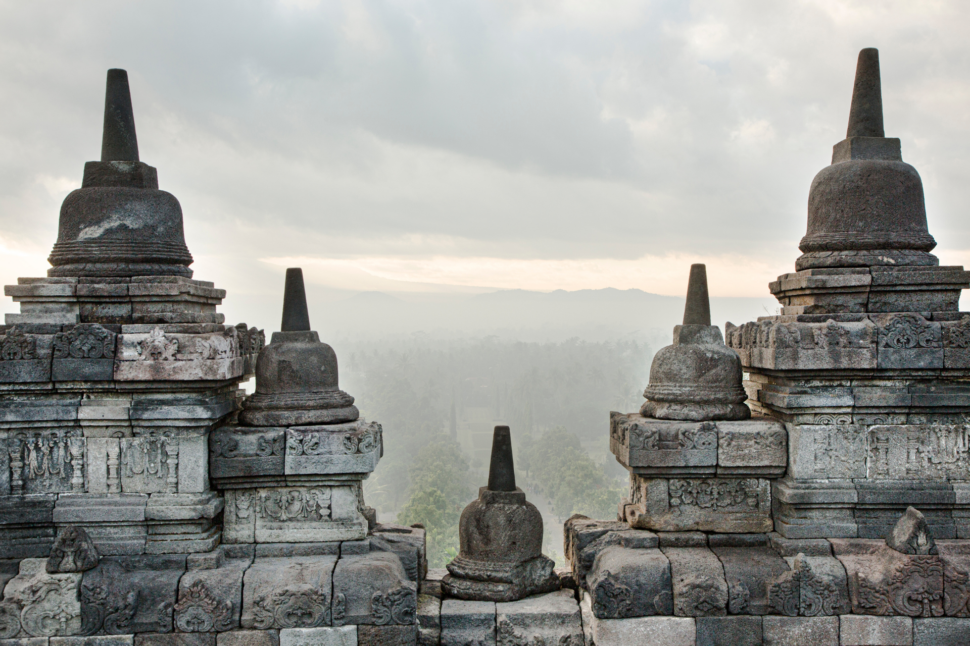 Borobudur's stone stupas with bell-shaped tops, silhouetted against a misty landscape.