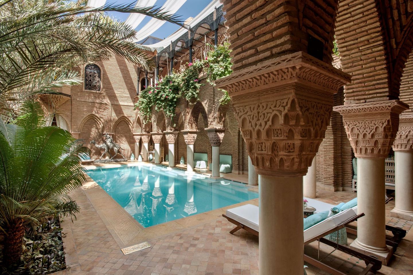 Riad pool beneath arched brick colonnades and palm trees in a sunlit atrium