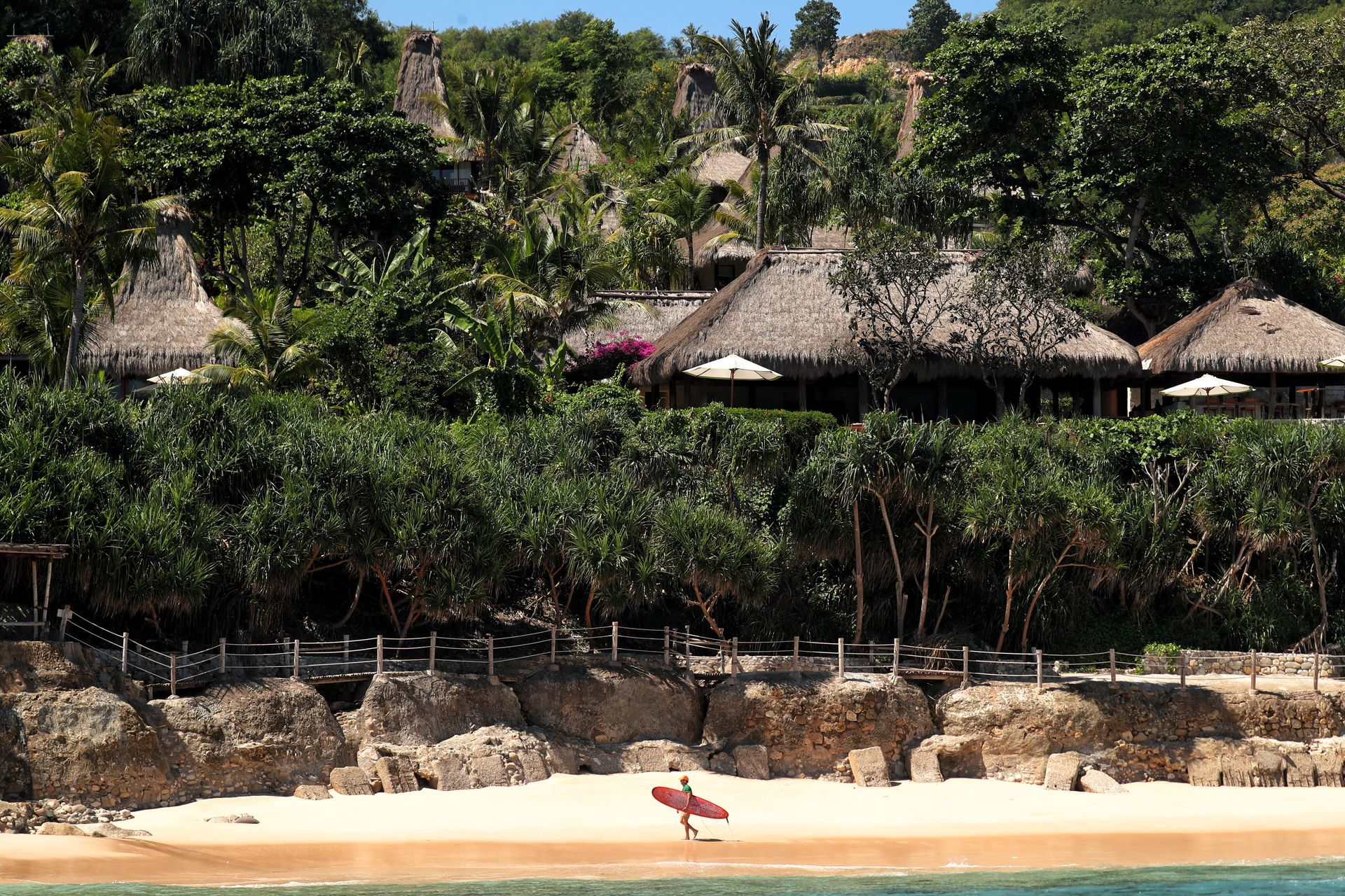Tropical Indonesian beach with thatched huts, dense greenery, and a lone red umbrella on the sand