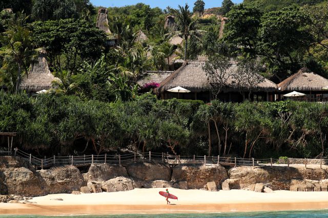 Tropical Indonesian beach with thatched huts, dense greenery, and a lone red umbrella on the sand