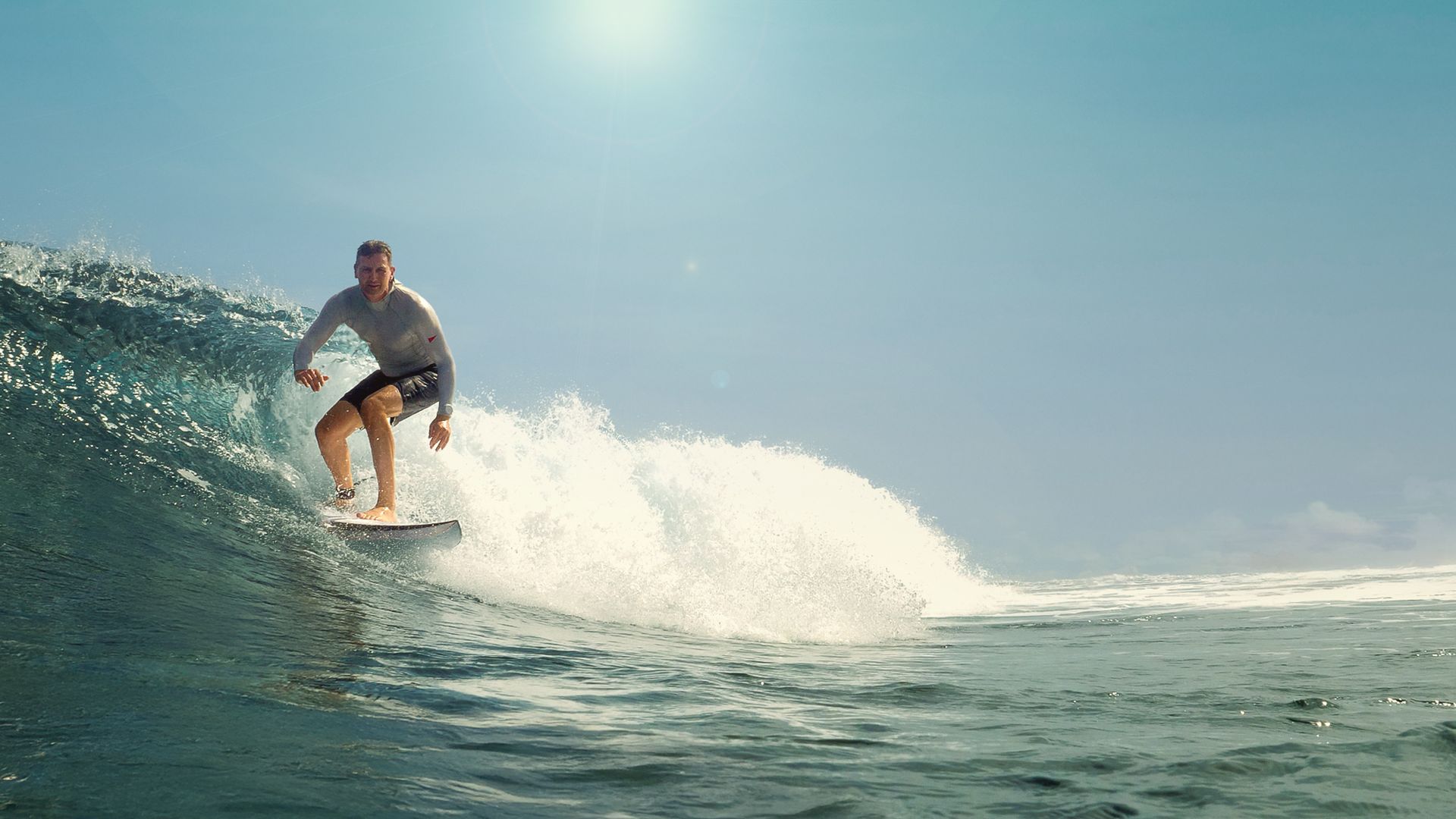 Surfer riding a wave under a bright blue sky, splashing through the ocean