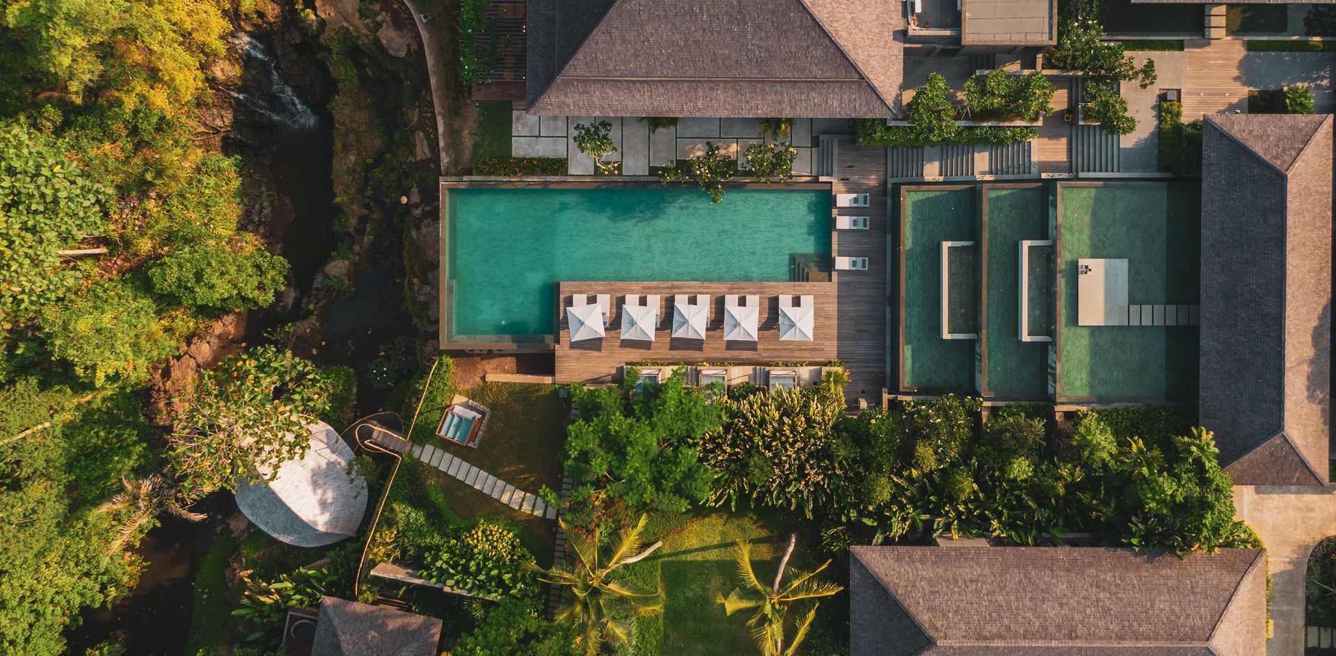 Aerial view of a resort with a turquoise pool, sunbeds, and green landscaping.