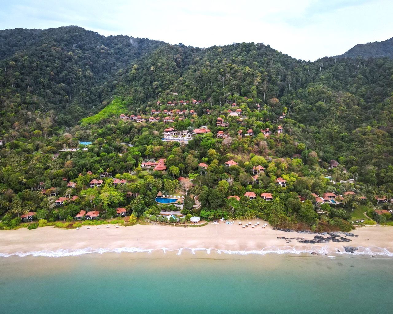 An aerial view of a beach surrounded by mountains and trees.
