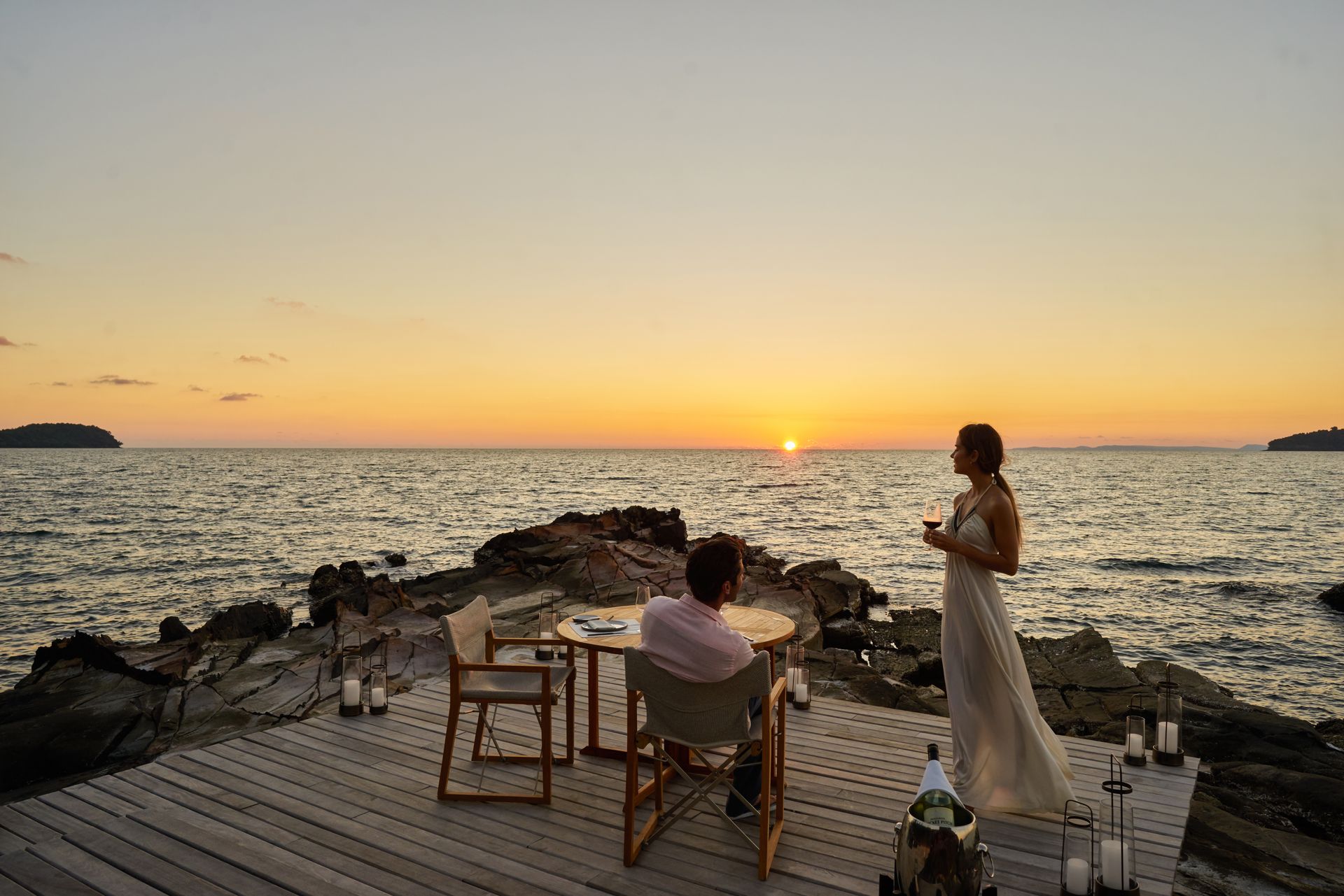 A man and a woman are sitting at a table by the ocean at sunset.
