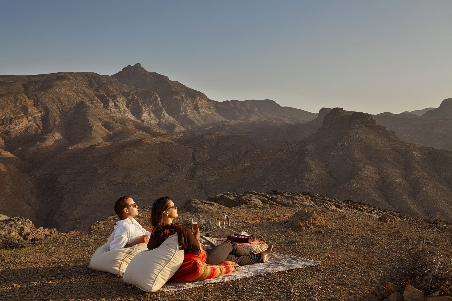 Two people are sitting on a blanket on top of a mountain.