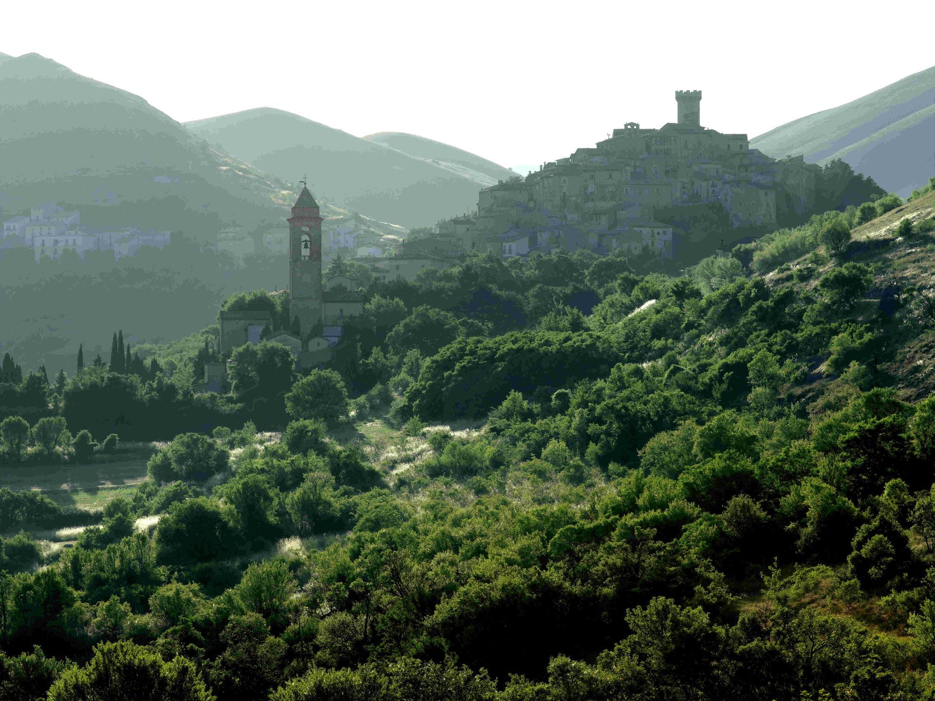 A lush green landscape with a village atop a hill, a tall bell tower and castle tower.