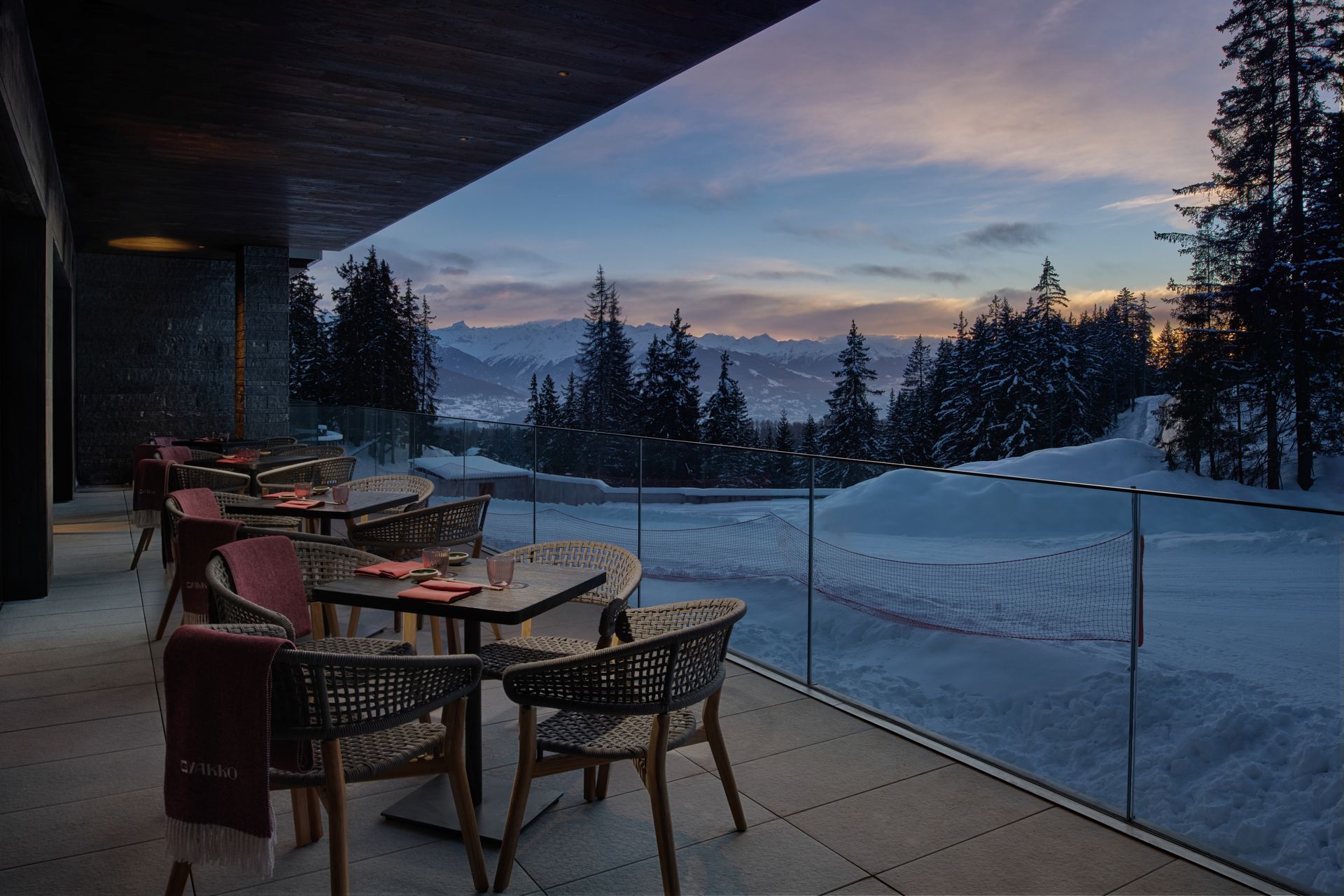 A balcony with tables and chairs overlooking a snowy forest.