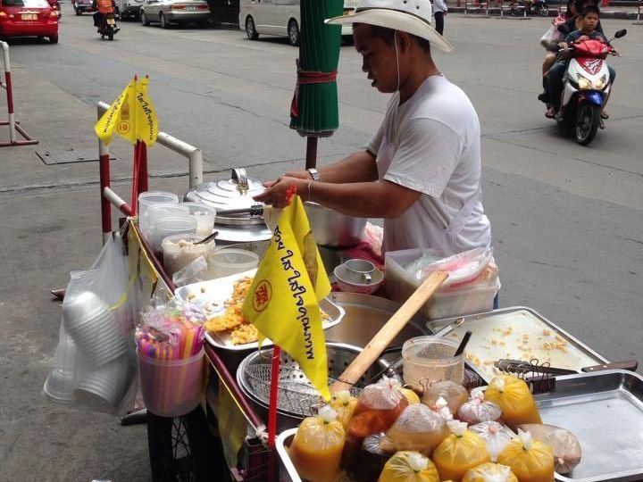 A man is standing behind a cart with a yellow flag that says ' thailand ' on it