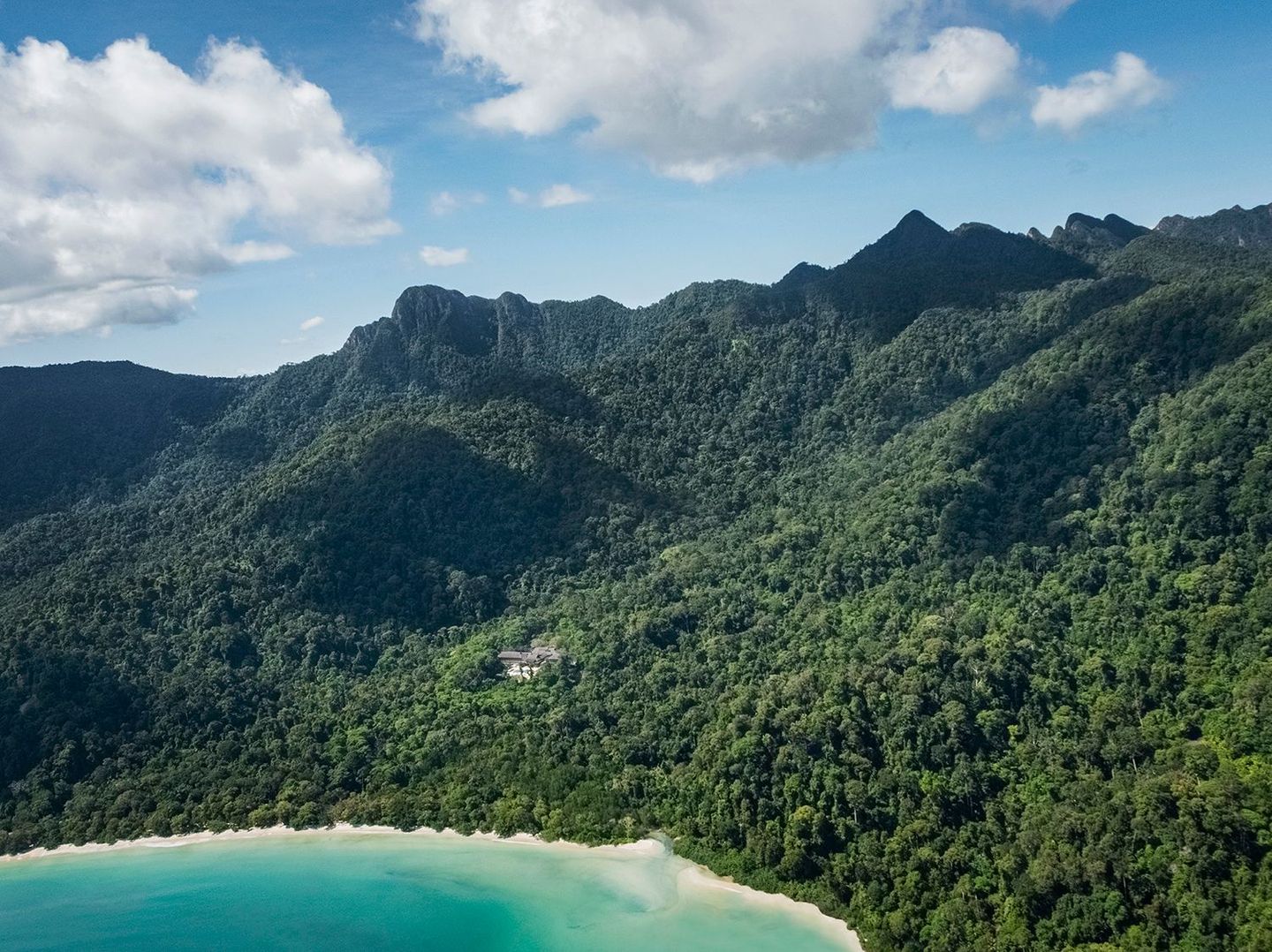 Tropical coastline with turquoise water, sandy beach, and lush jungle mountains under a cloudy sky