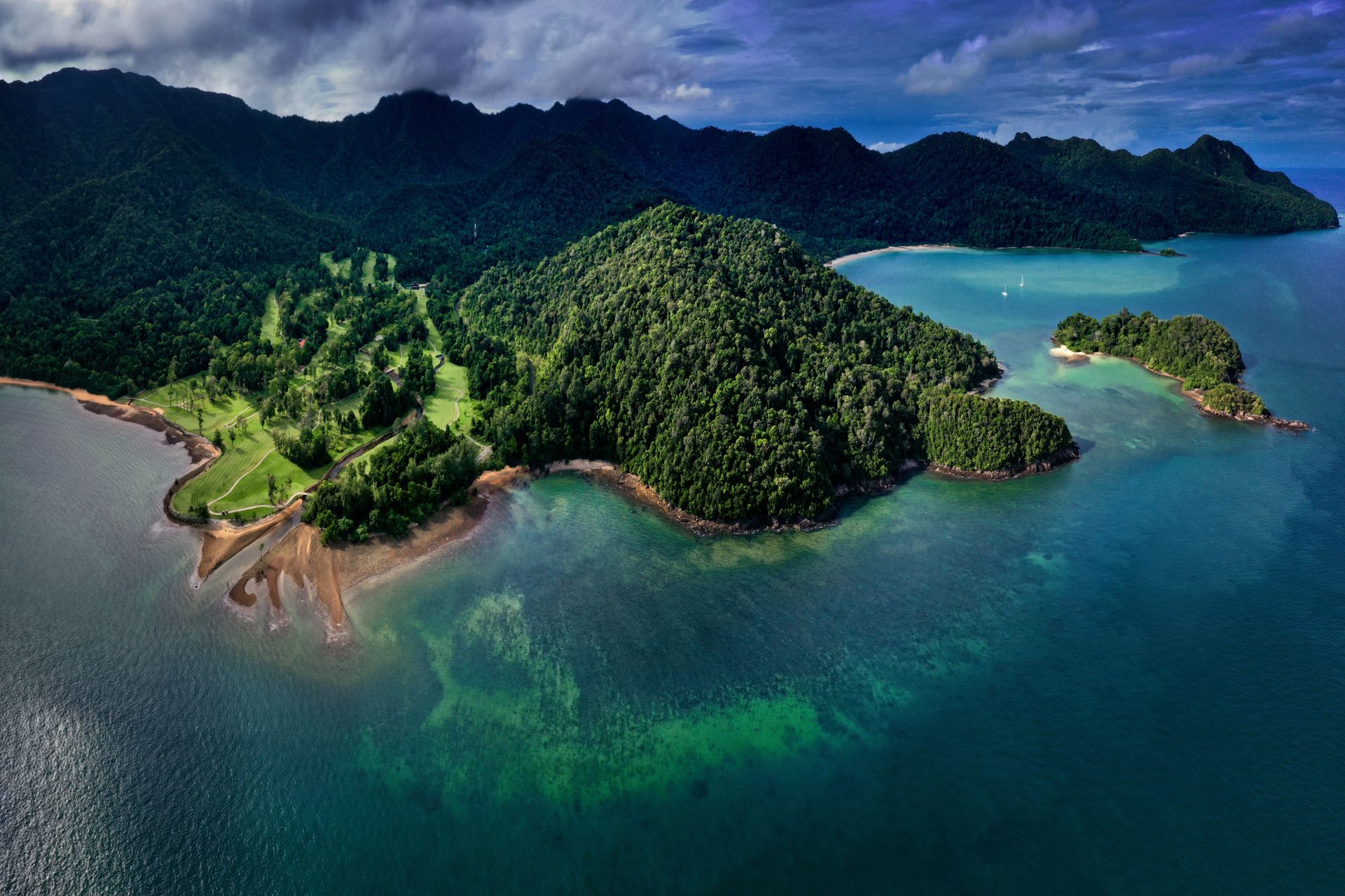 Aerial view of lush green tropical Malaysian islands surrounded by turquoise ocean and dark clouds