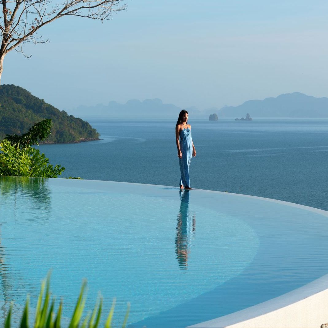 A woman is standing on the edge of an infinity pool overlooking the ocean.