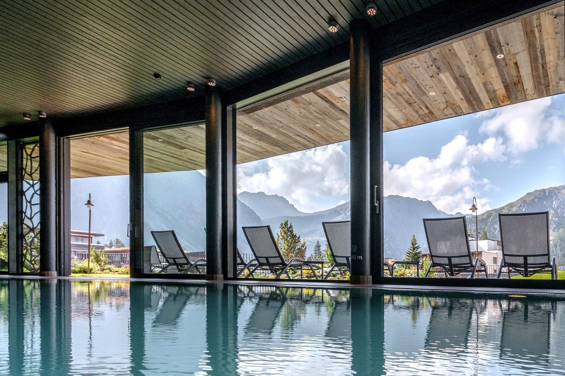 Valsana's Indoor pool with mountain view, lounge chairs, and reflection in the water.