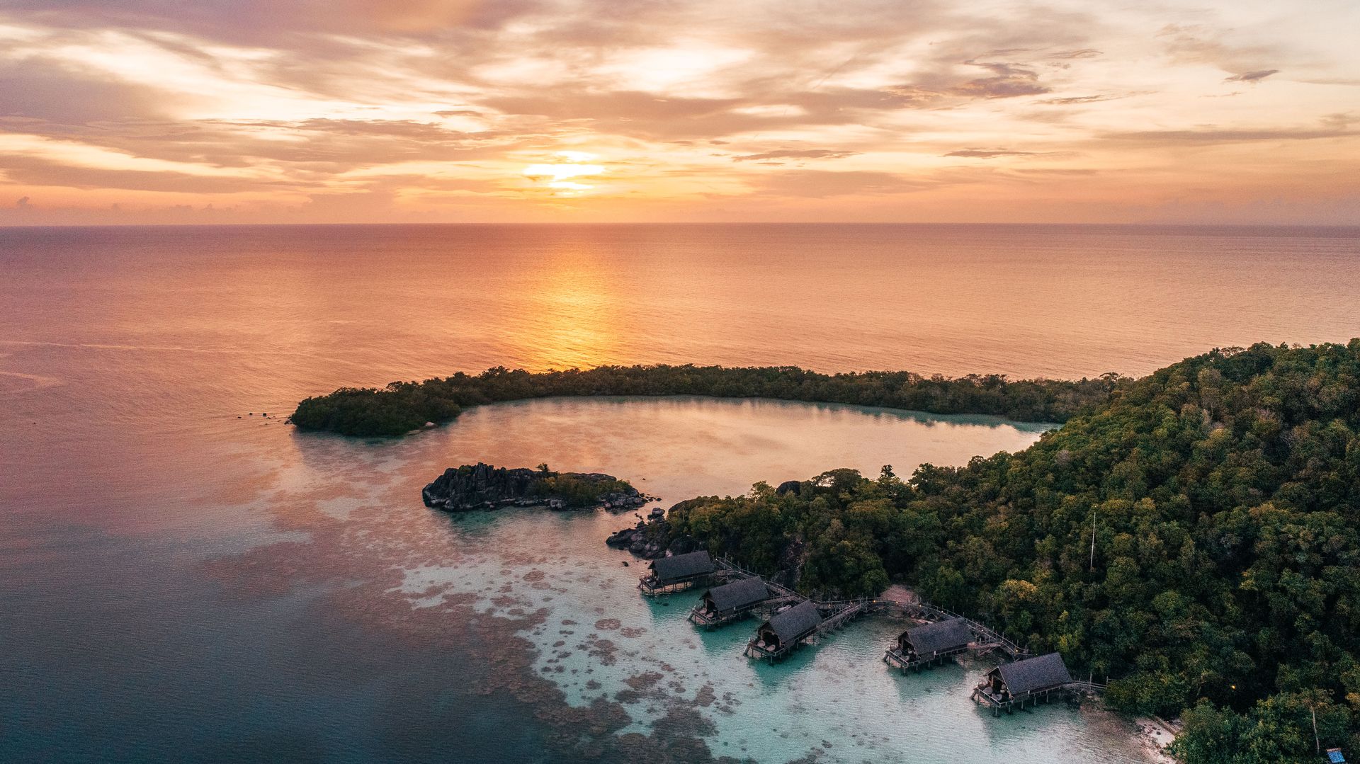An aerial view of a small island in the middle of the ocean at sunset.