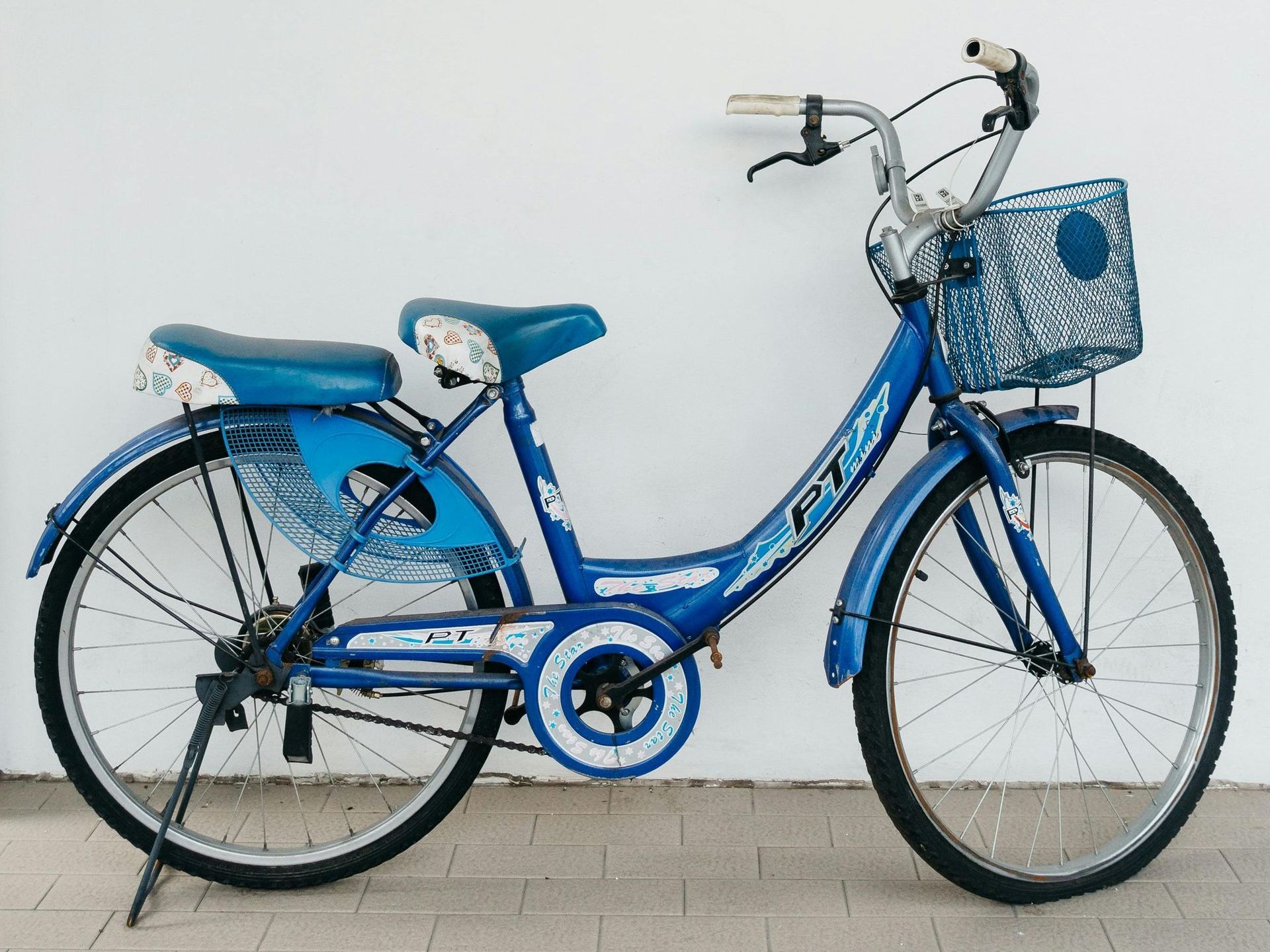 A blue bicycle with a basket is parked in front of a white wall