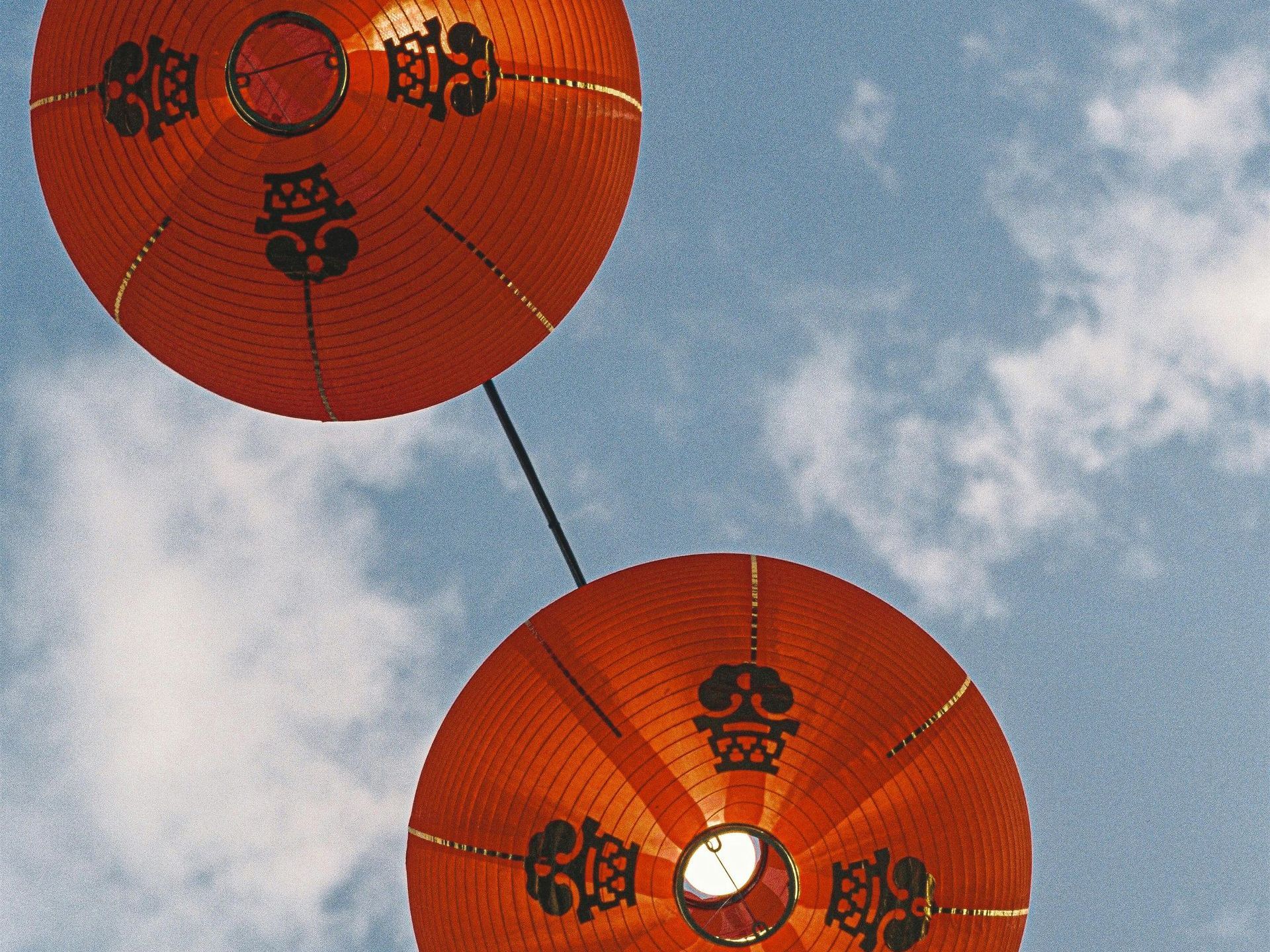 Two orange lanterns with chinese writing on them against a blue sky