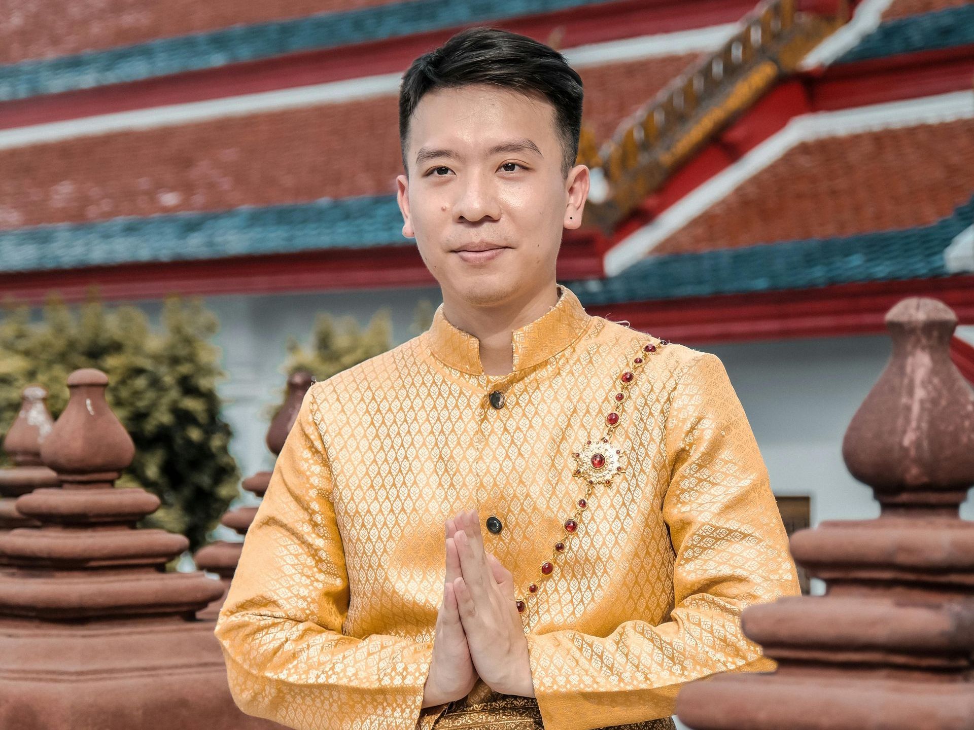 A man in a yellow shirt is standing in front of a building with his hands folded.