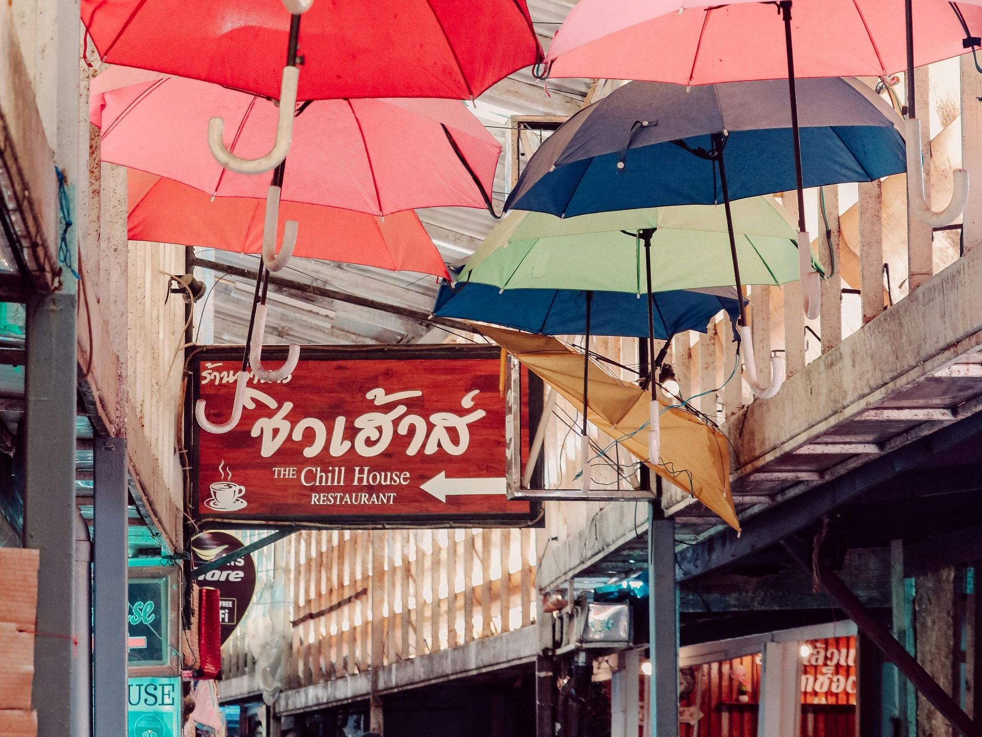 A sign for a restaurant is surrounded by umbrellas hanging from the ceiling.