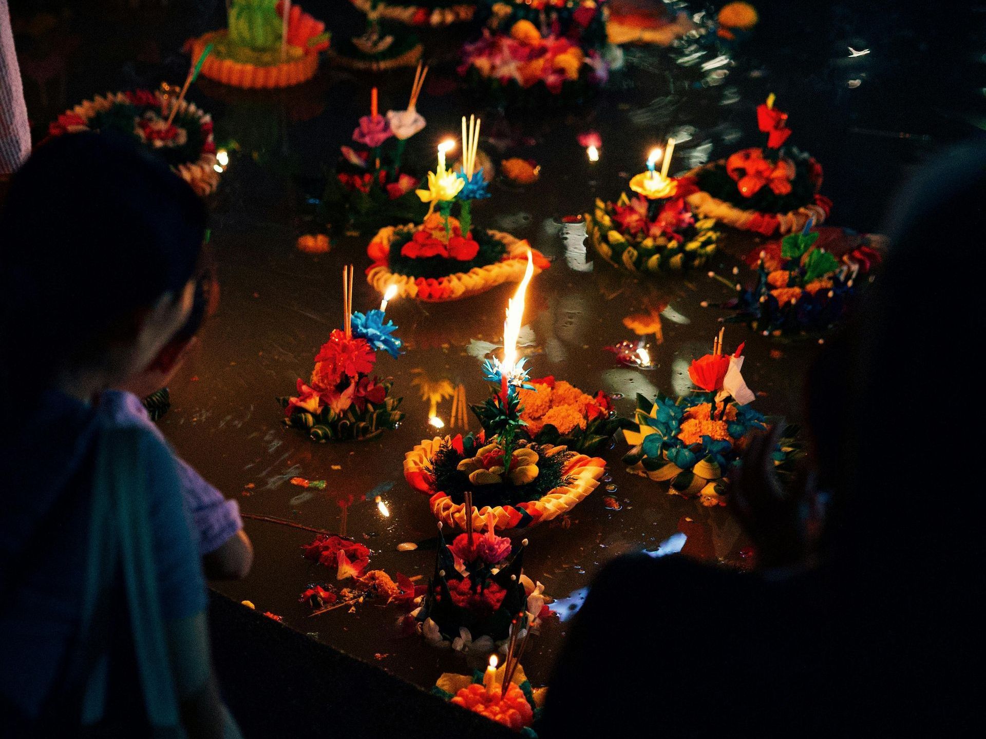 A group of people are looking at candles floating in the water