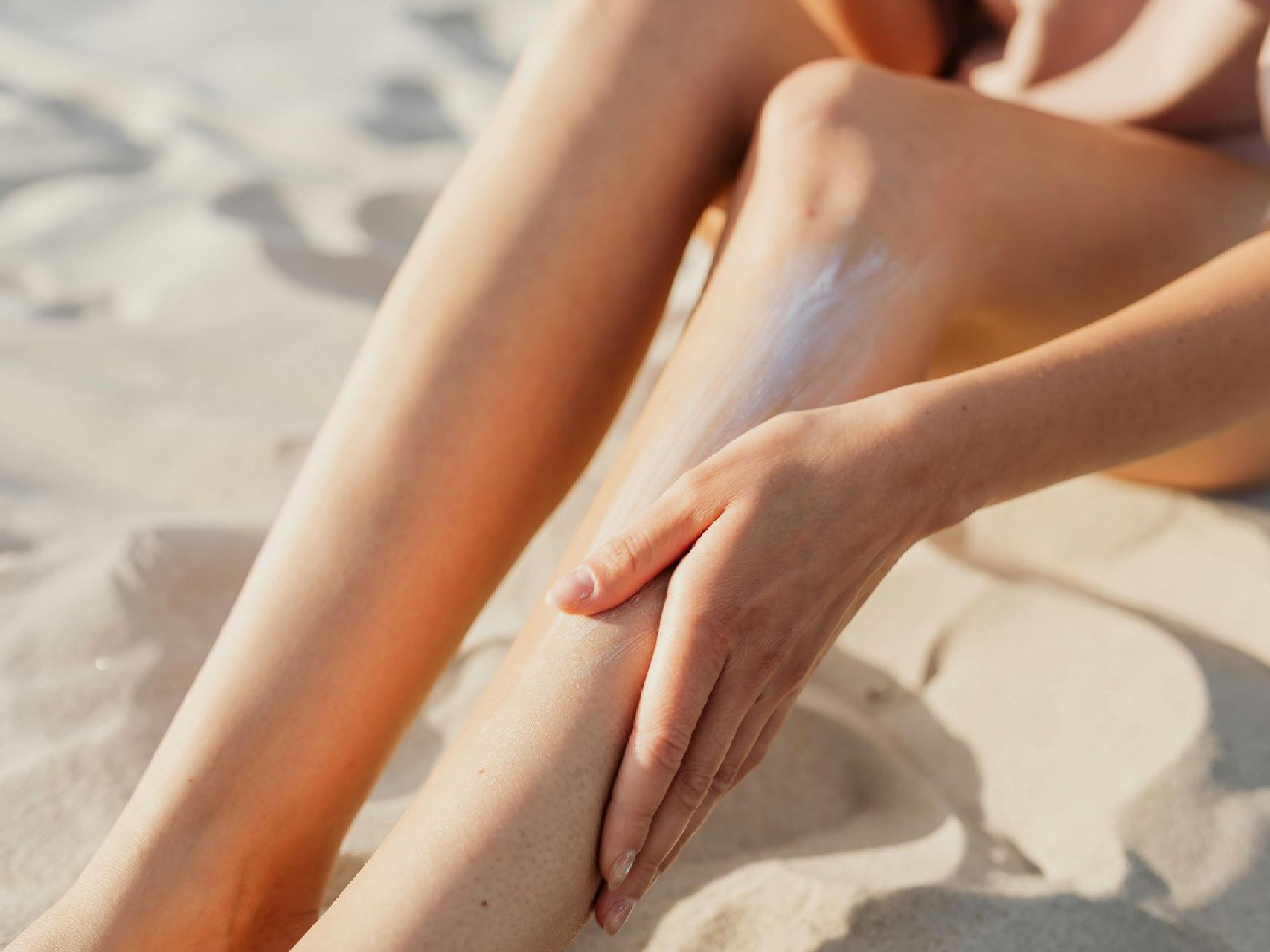 A woman is applying sunscreen to her legs on the beach.