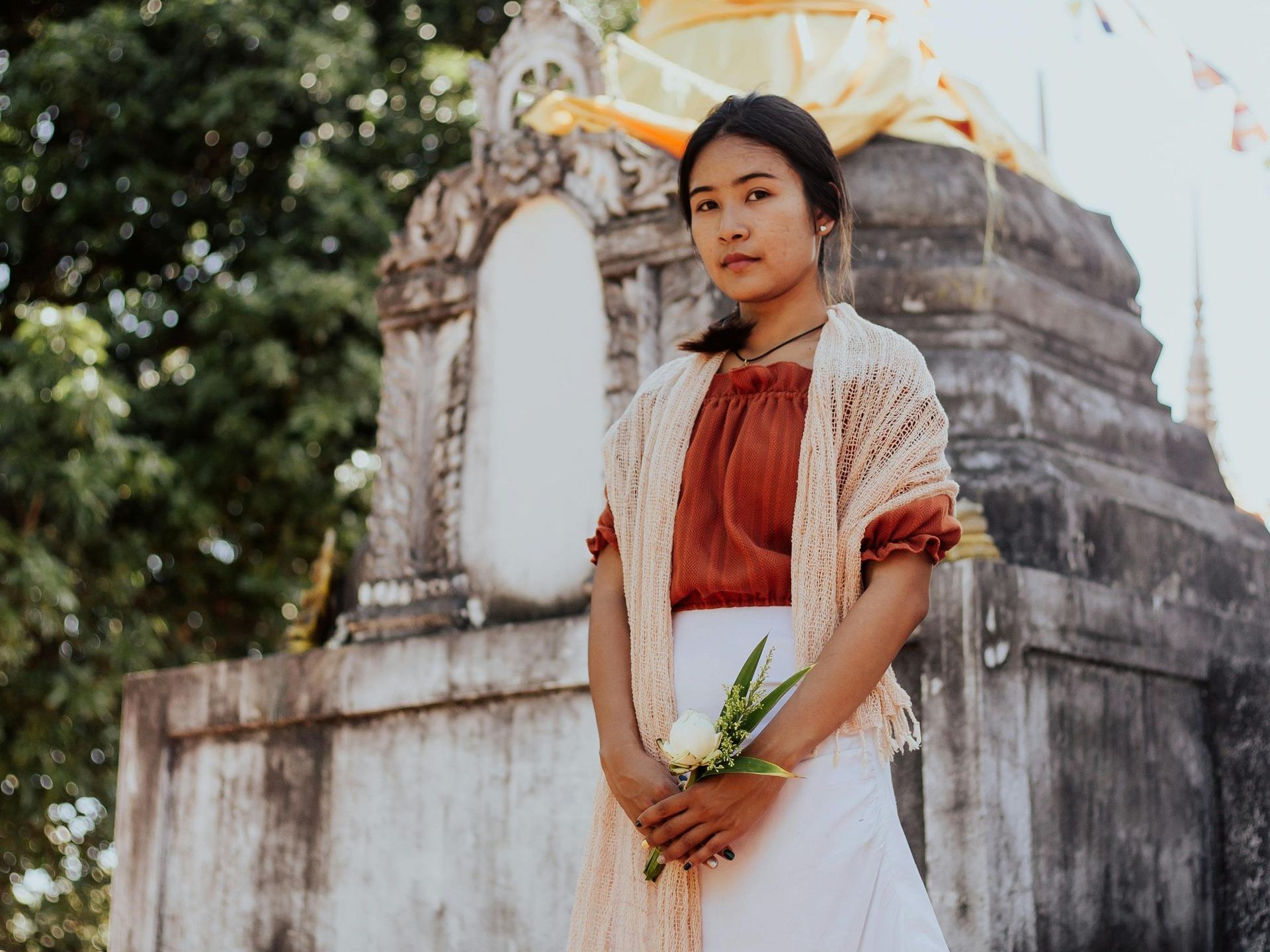 A woman is standing in front of a statue holding a flower.