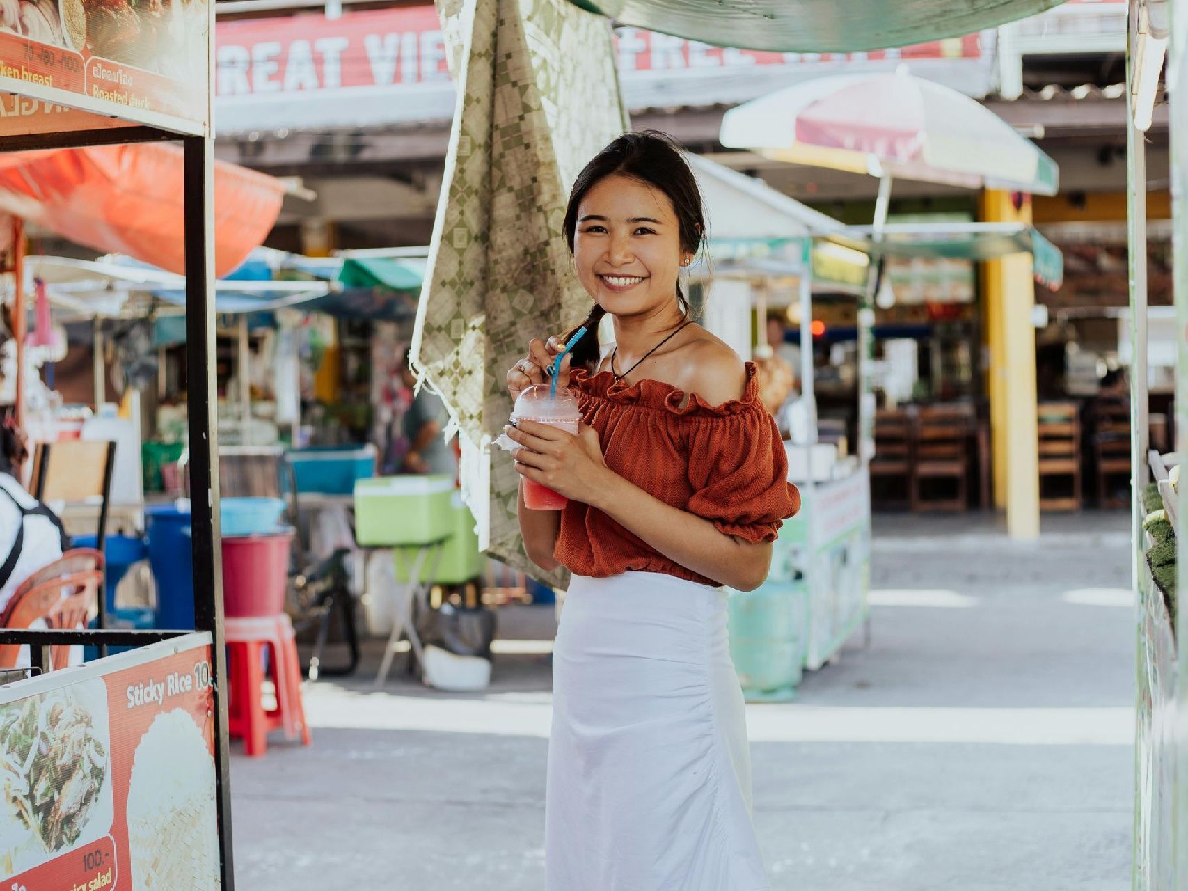 A woman is standing in front of a food stand holding a drink.