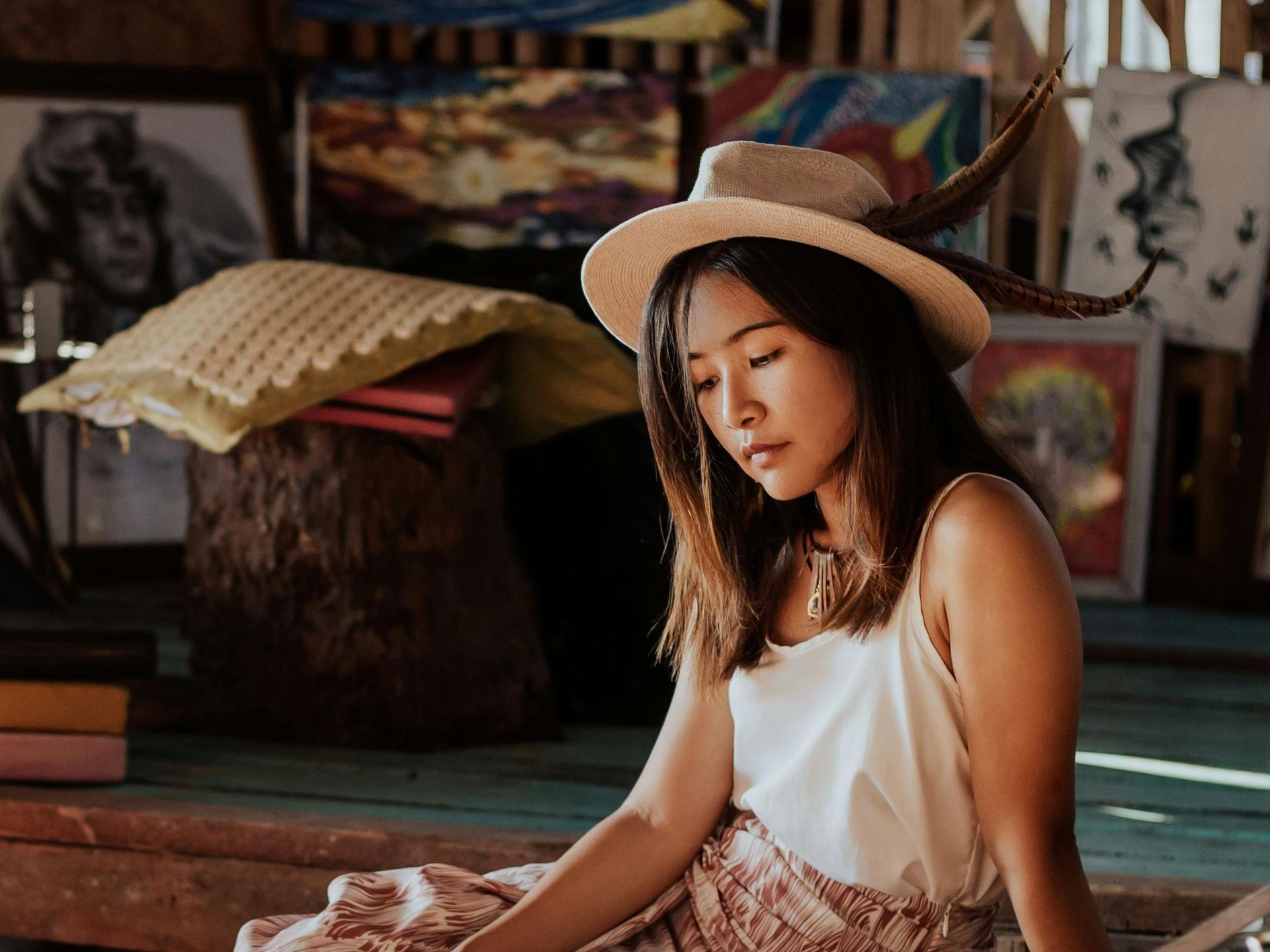 A woman wearing a hat is sitting on a bench with her eyes closed.