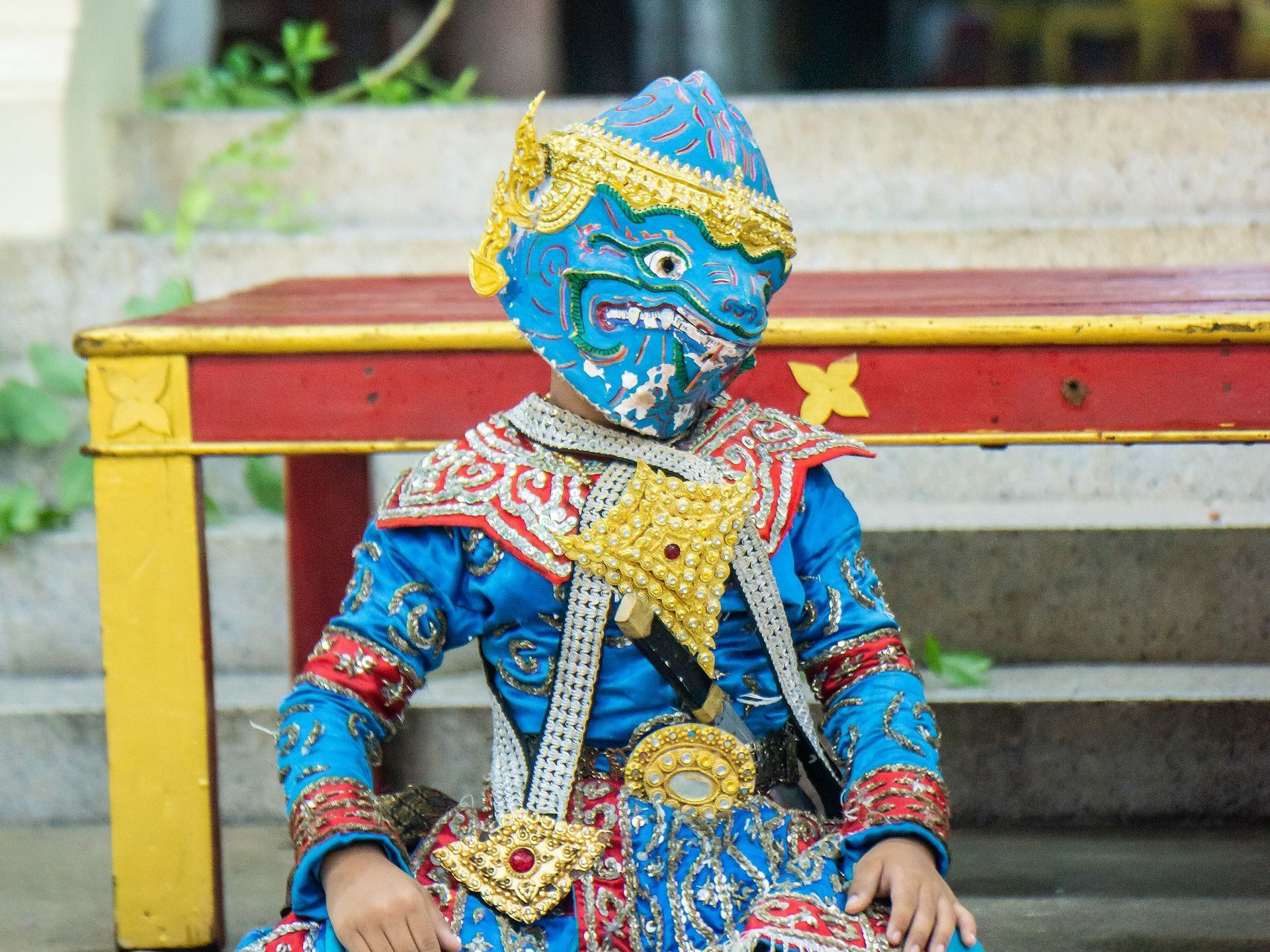 A person in a blue and gold costume is sitting on a bench.