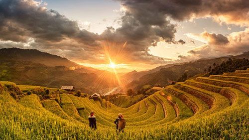 Sunset over terraced rice fields with two  farmers cultivating their land