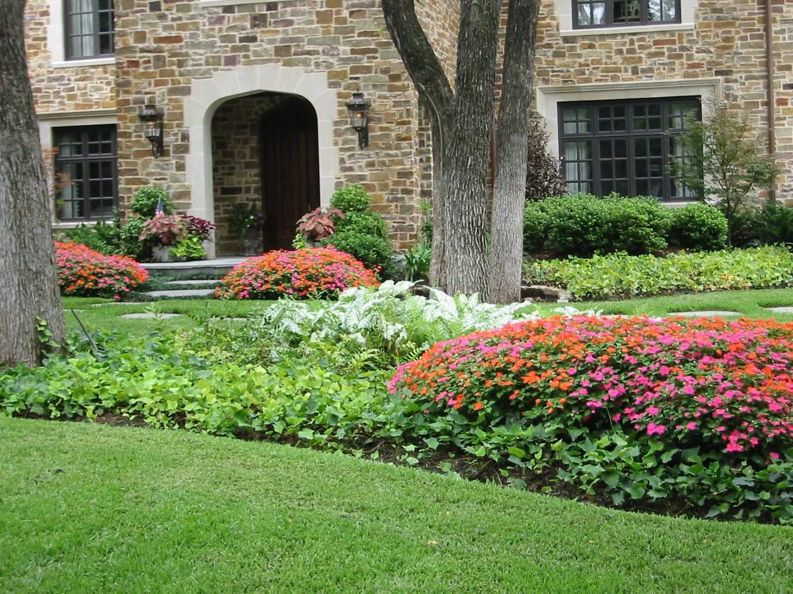 Stone house with lush landscaping, colorful flowers, and green lawn.