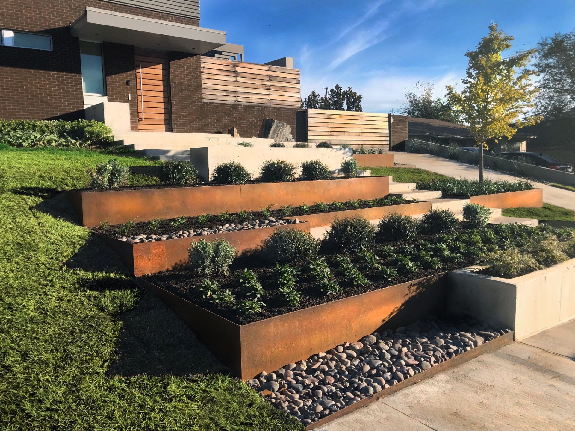 Modern home exterior with tiered, rusty metal planters filled with plants and gravel.