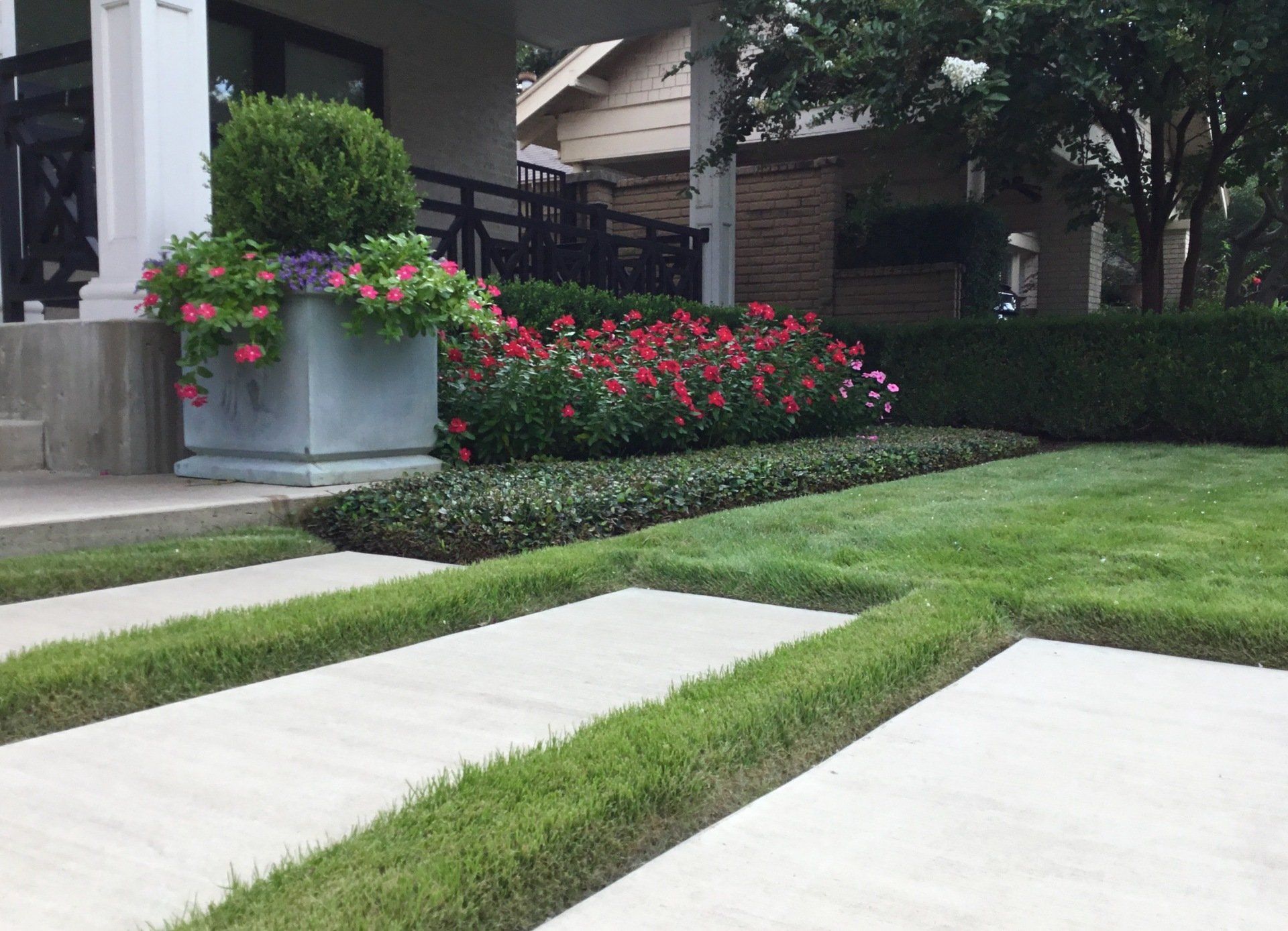 Concrete driveway with grass strips and flower bed in front of a house.