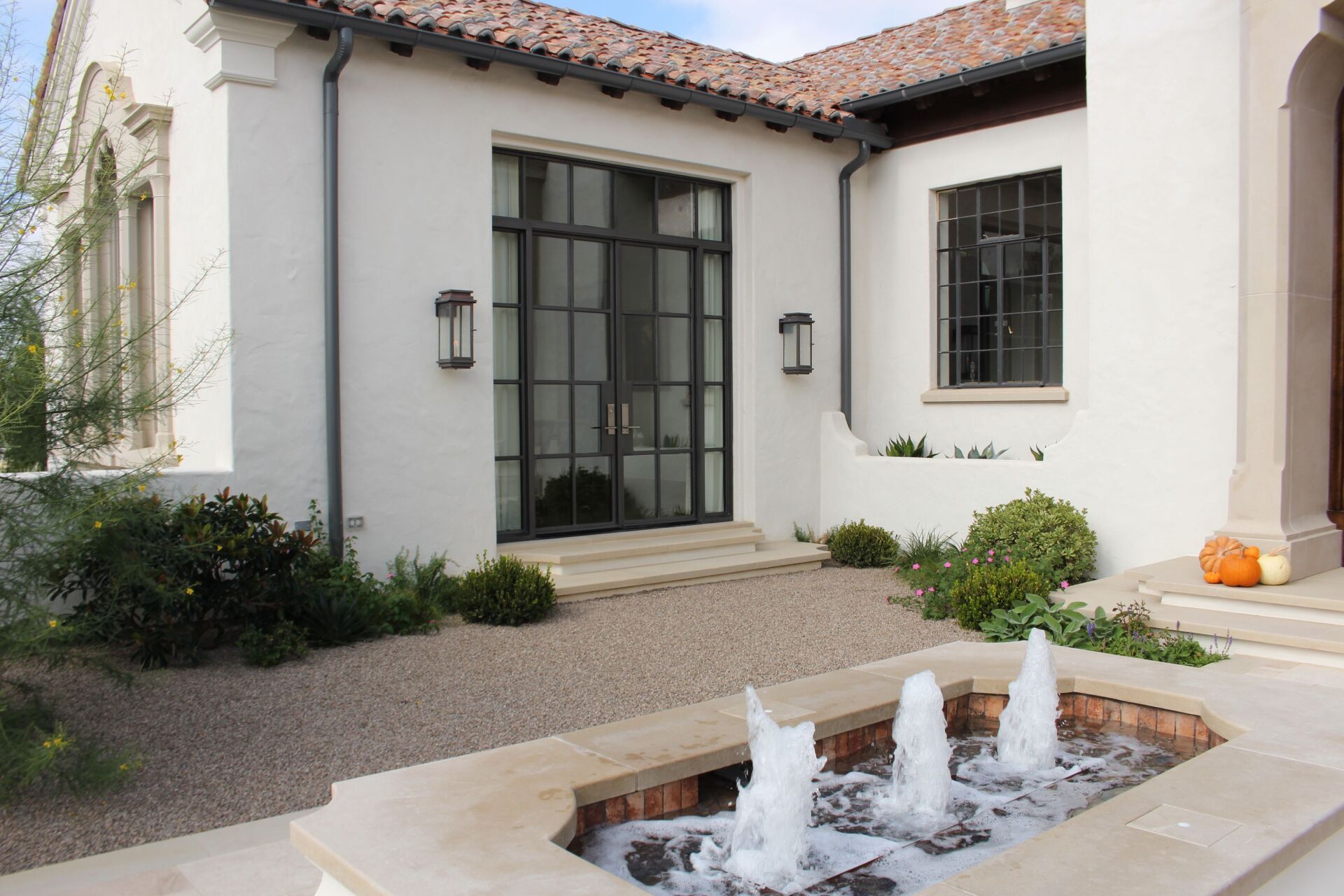 Exterior of white stucco home with black framed doors and windows, water fountain, and landscaping.