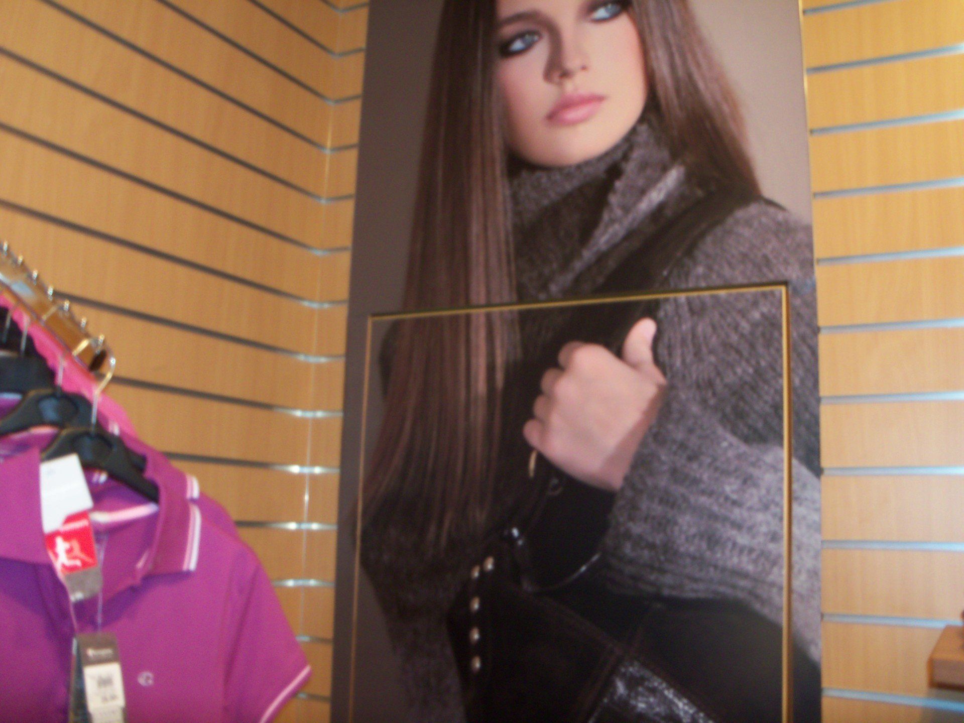 Donna con cappotto grigio e borsa nera in mano. In un negozio, con espositore di vestiti.