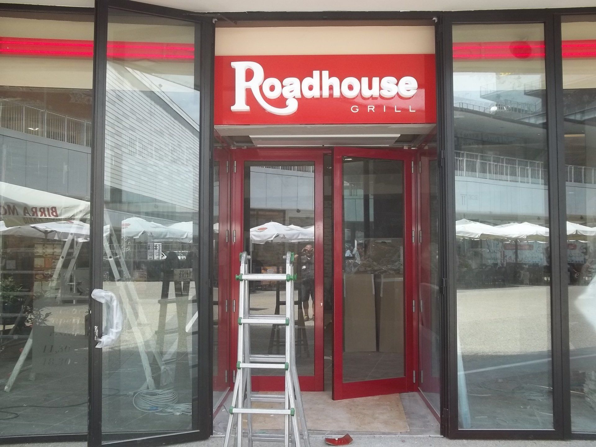Ingresso del Roadhouse Grill con rifiniture rosse, insegna e scala. Posti a sedere all'aperto visibili sullo sfondo.