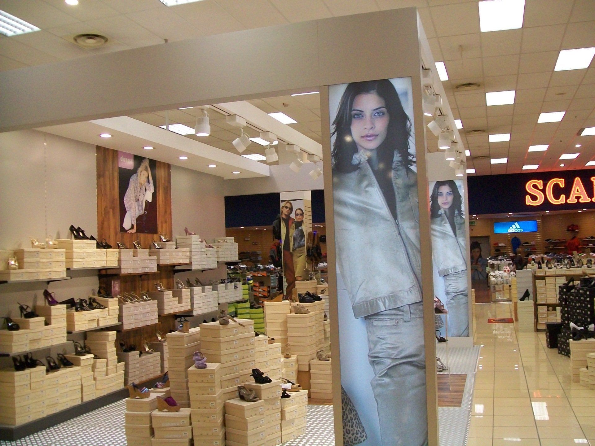 Interno di un negozio di scarpe con espositori di legno impilati e grandi poster pubblicitari raffiguranti una donna che indossa abiti.