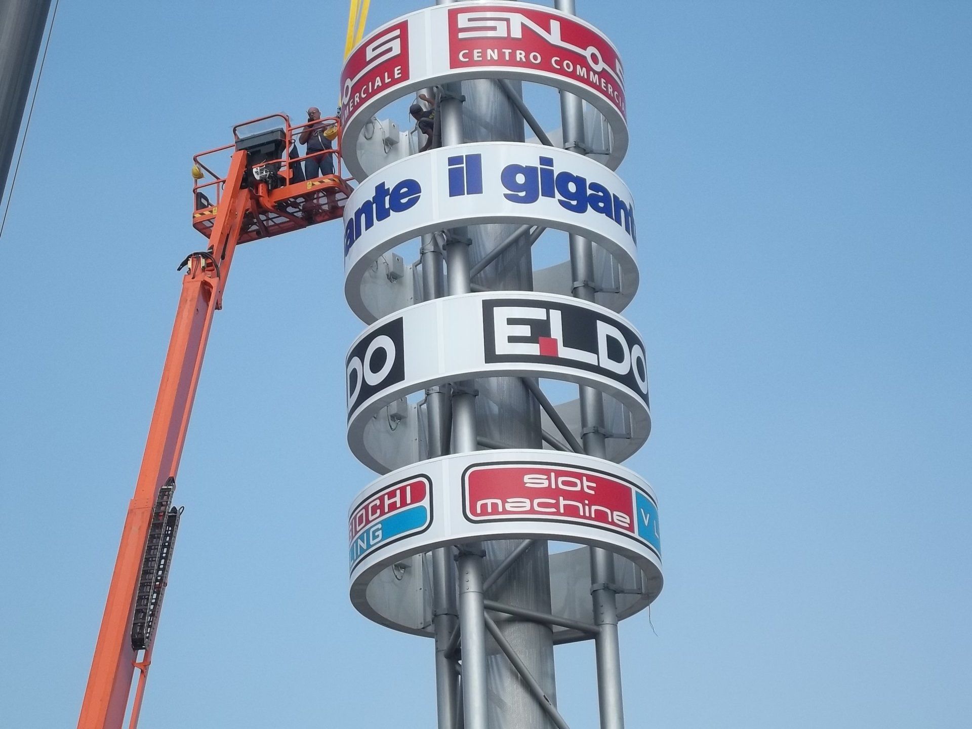 Costruzione di un'alta insegna con pannelli pubblicitari circolari; operai in un ascensore.