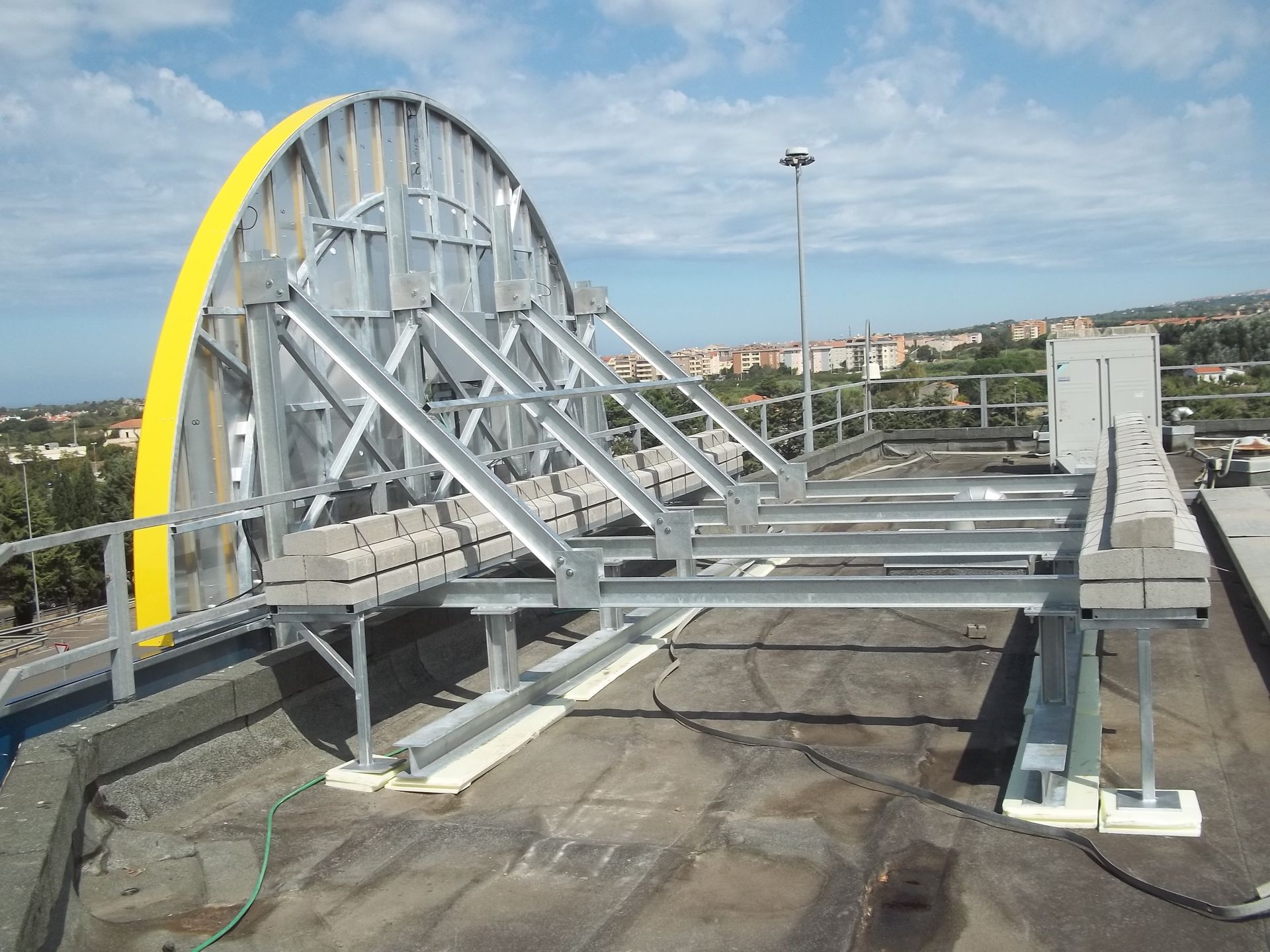 Struttura in acciaio su un tetto con un arco giallo che sostiene un cartellone pubblicitario. Sullo sfondo lo skyline della città.