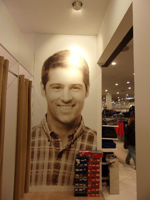 Il volto sorridente di un uomo che indossa una camicia a quadri è raffigurato su una parete di un negozio di abbigliamento.