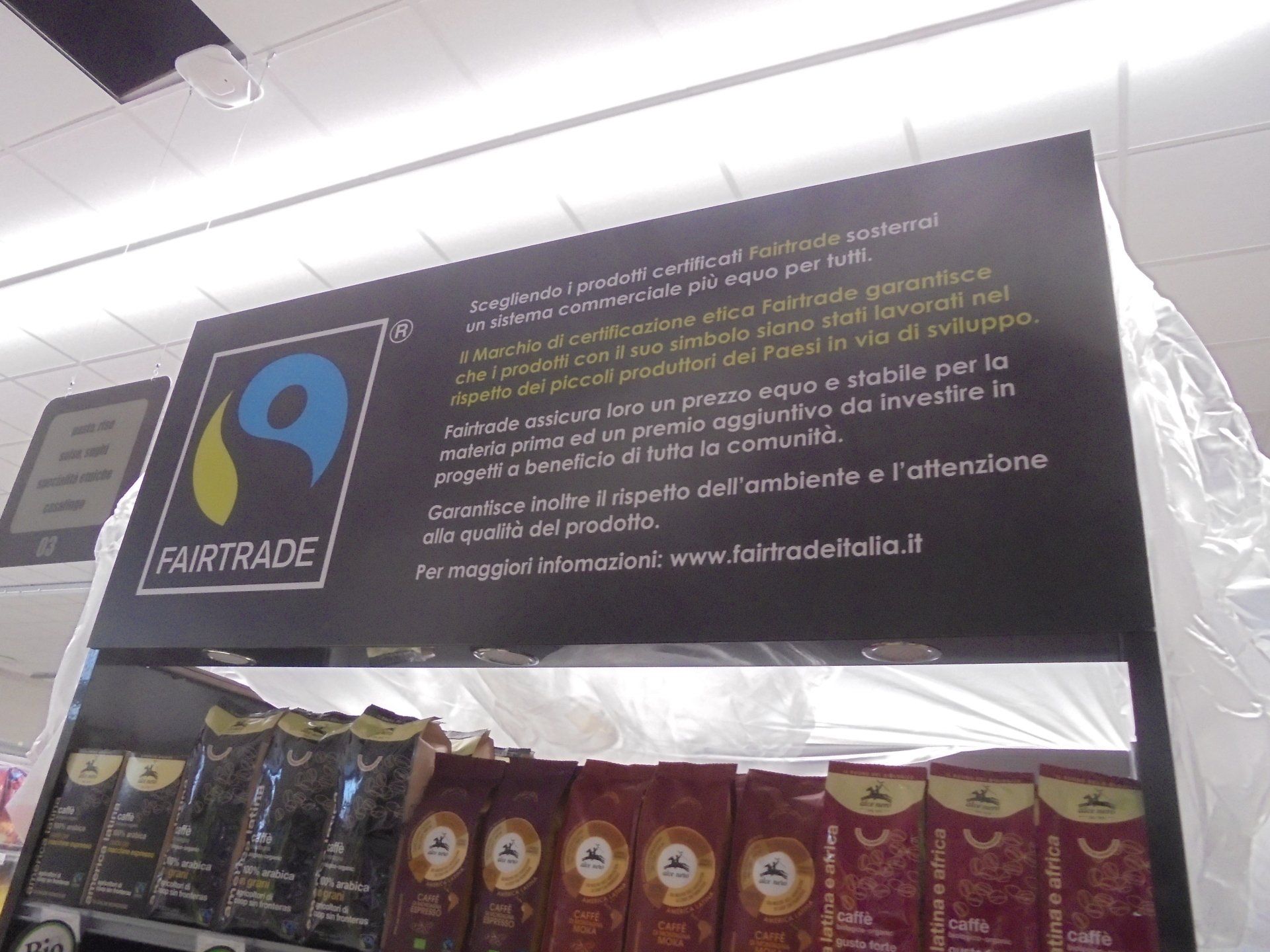 Esposizione di caffè Fairtrade in un negozio. Insegna scura con logo e testo sopra le buste di caffè.