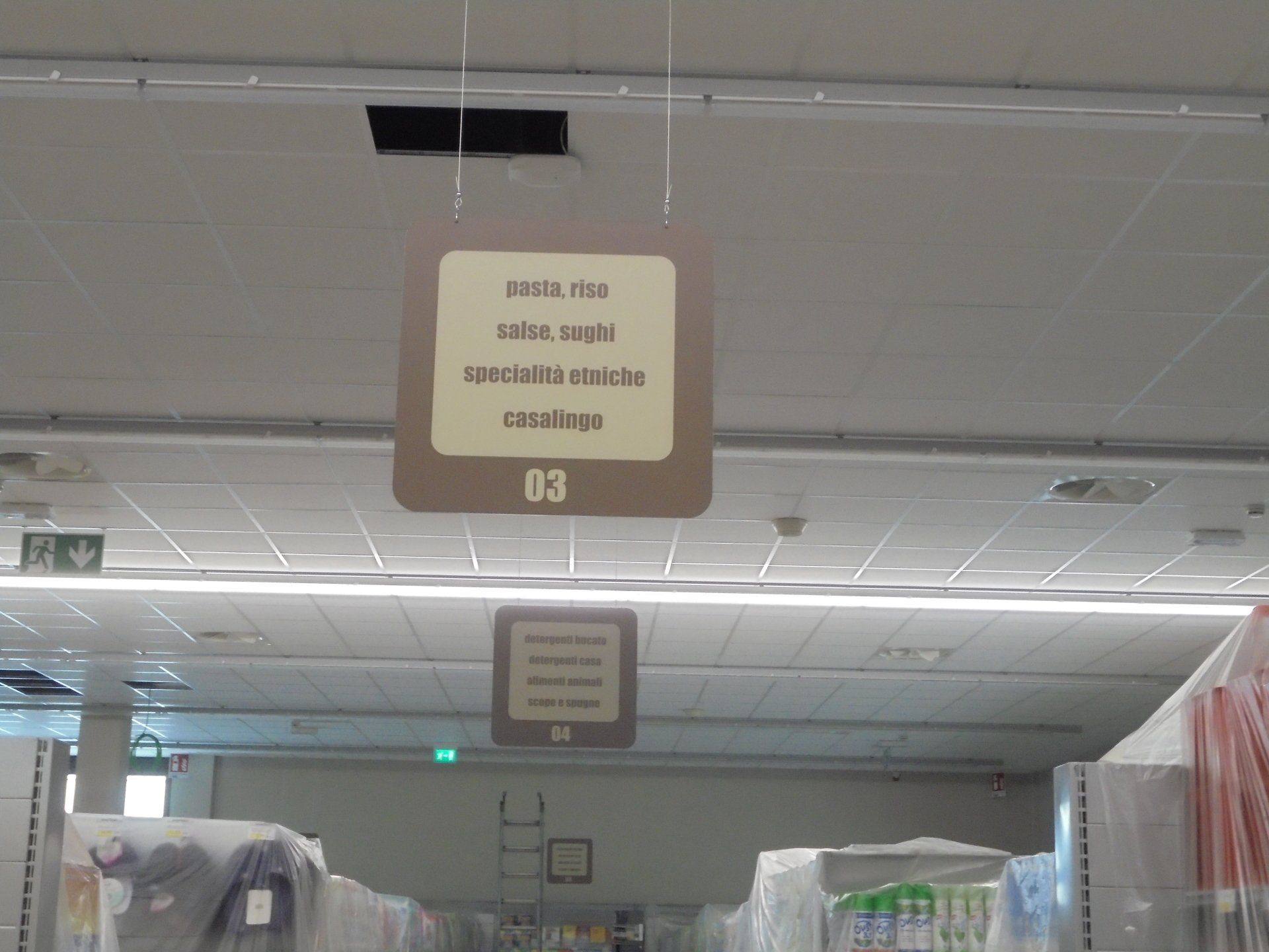 Due cartelli appesi con del testo in un negozio; sullo sfondo si vedono gli scaffali con i prodotti.