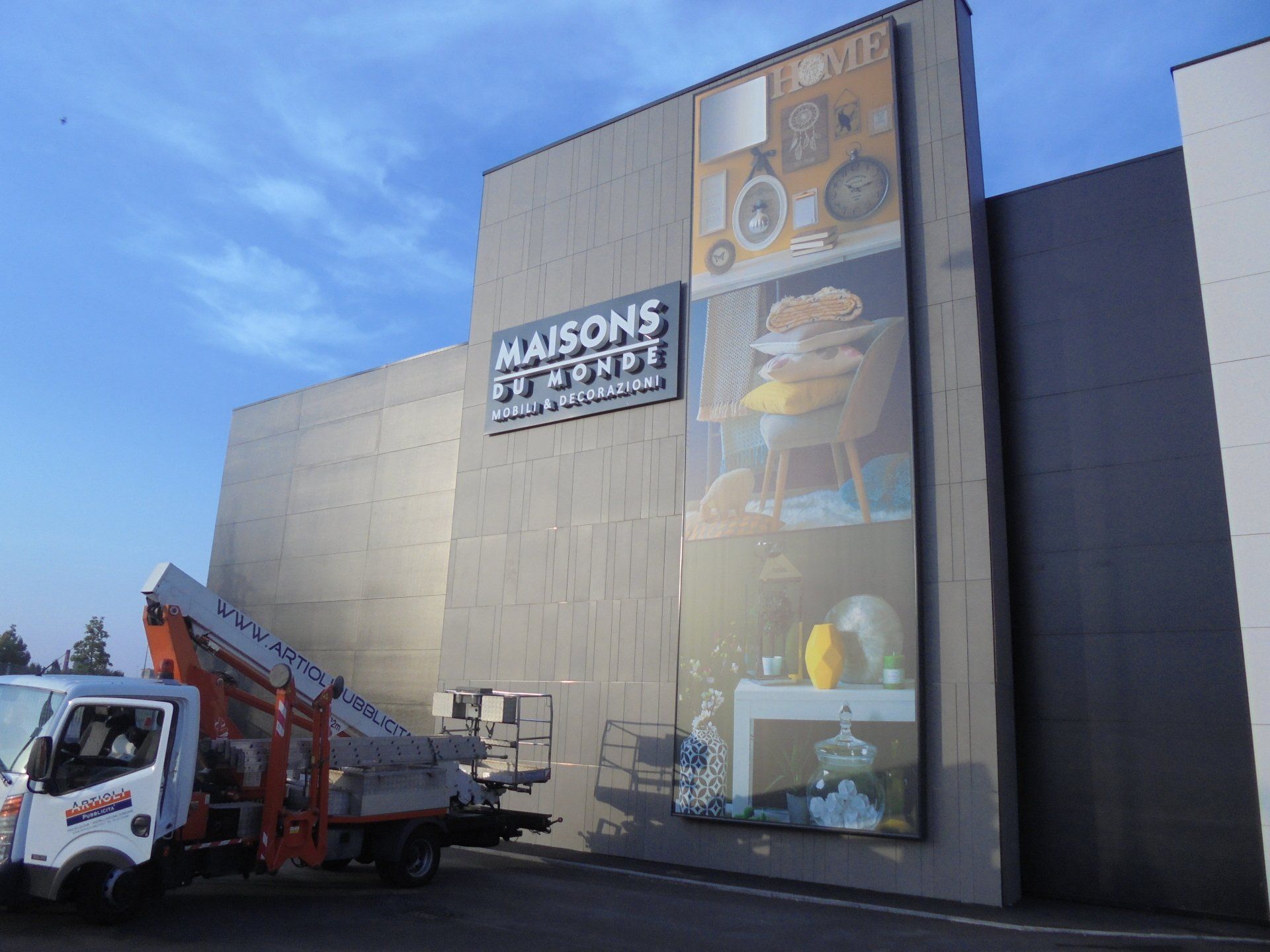 Negozio MAISONS DU MONDE con grande espositore pubblicitario; carrello elevatore di fronte.