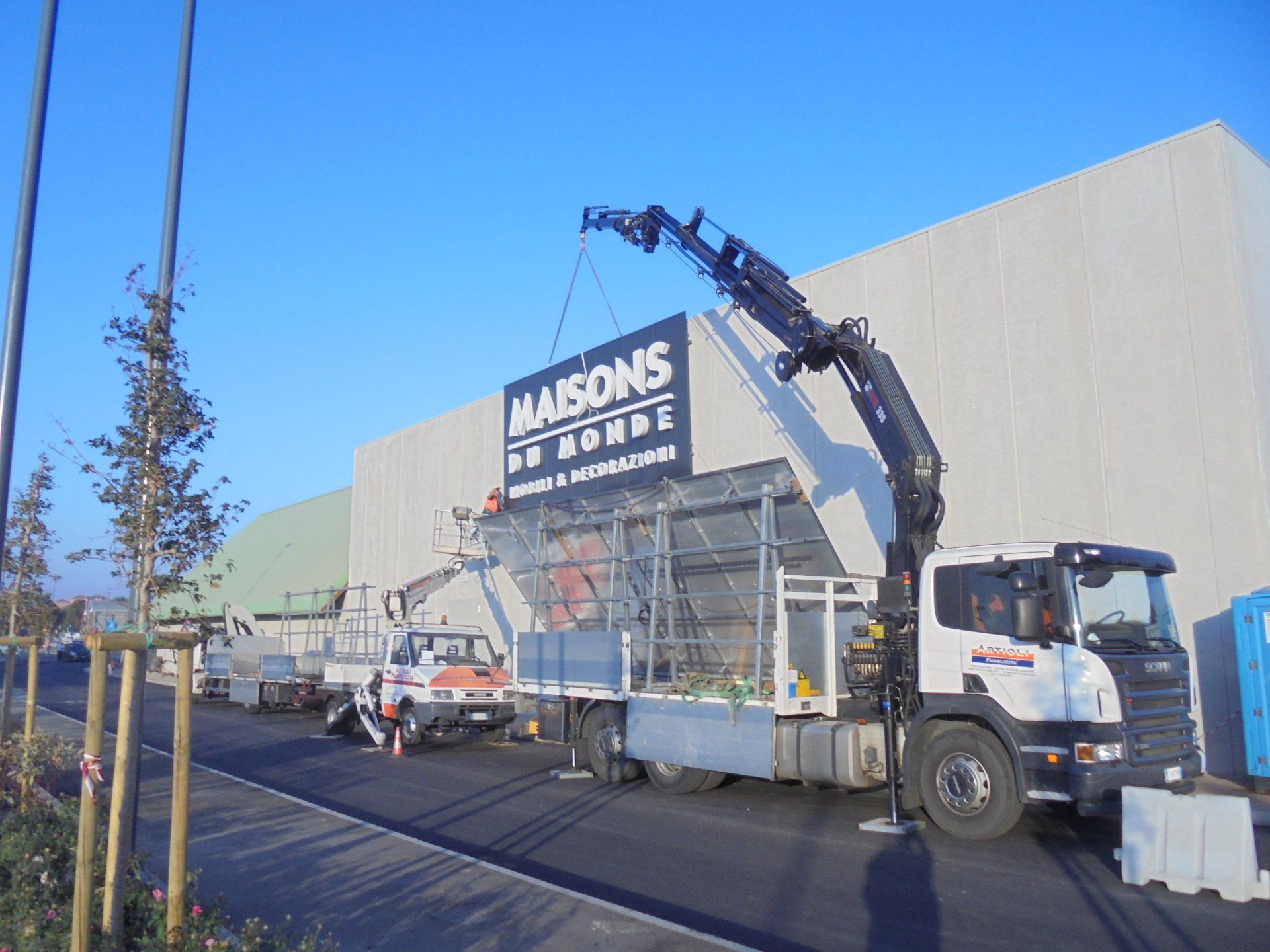 Un camion con gru solleva un cartello con la scritta 