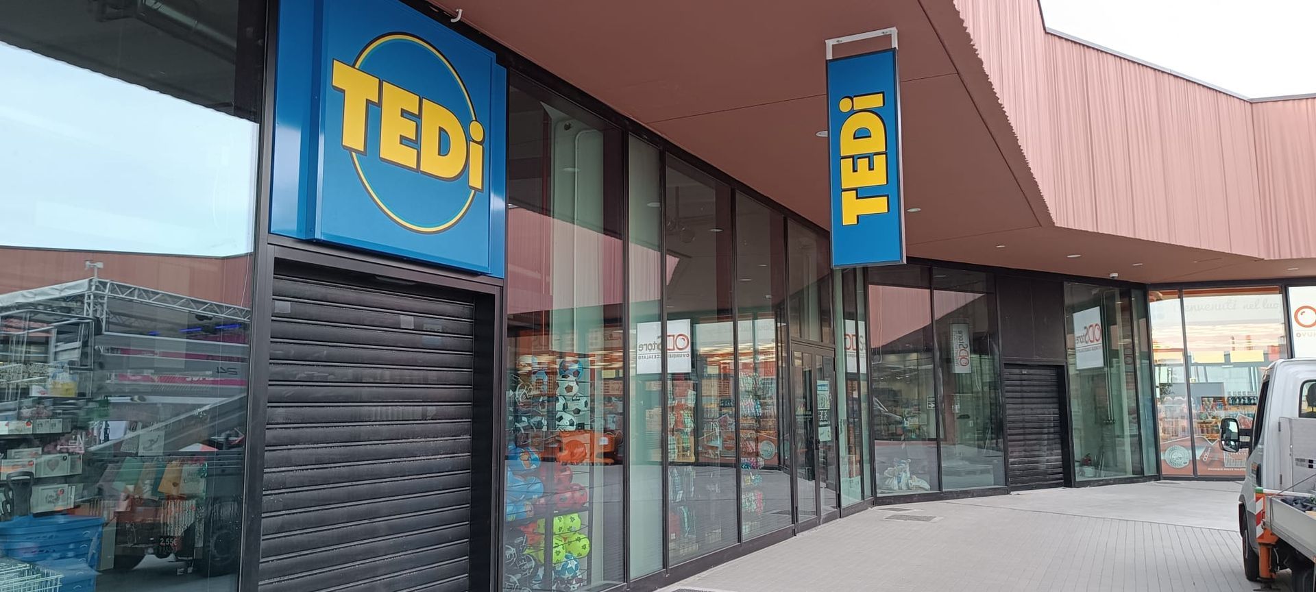 Negozio TEDI con logo blu e giallo. Serranda di sicurezza chiusa. Vista esterna.
