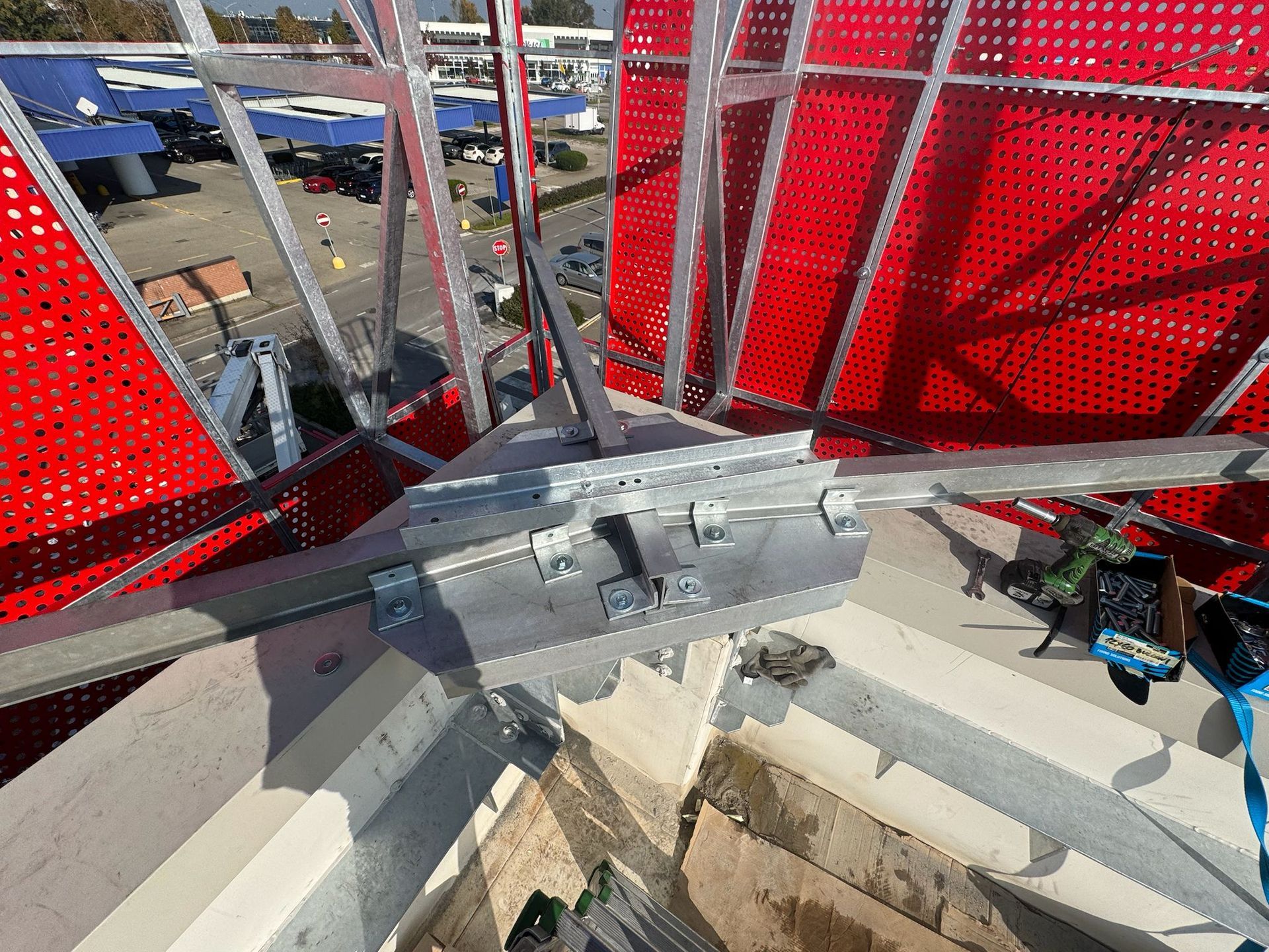 Primo piano della struttura metallica con pannelli perforati rossi, bulloni e attacchi, all'esterno.