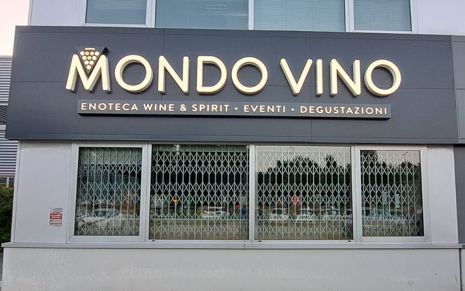 Insegna del negozio Mondo Vino con scritte dorate su sfondo grigio. In basso, la scritta 