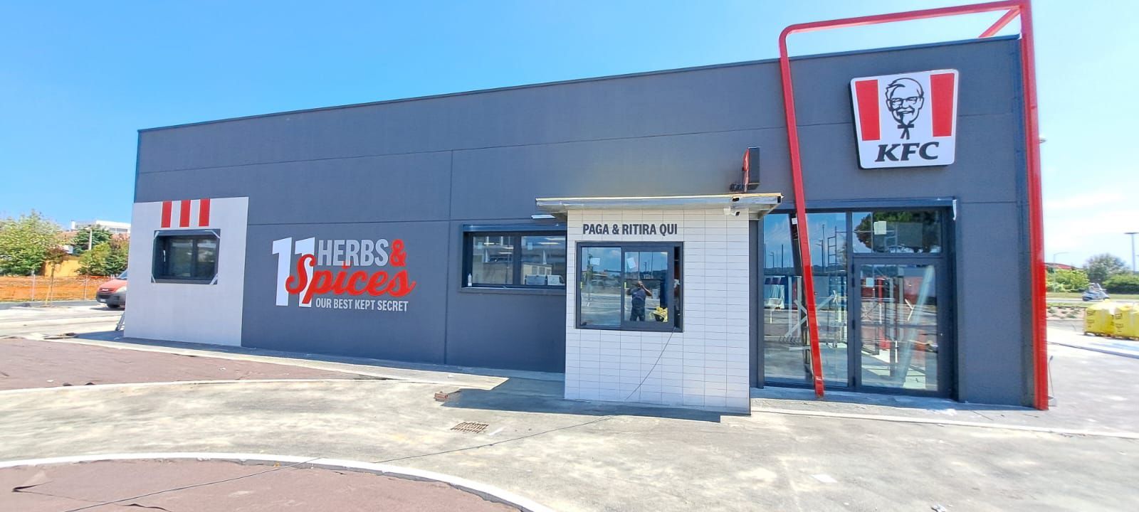 Esterno del ristorante KFC con sportello drive-through in una giornata di sole.