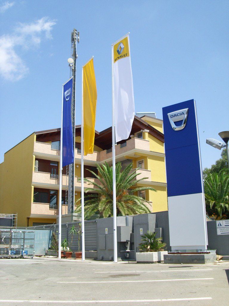 Bandiere e un cartello per le concessionarie Dacia e Renault davanti a un edificio giallo.