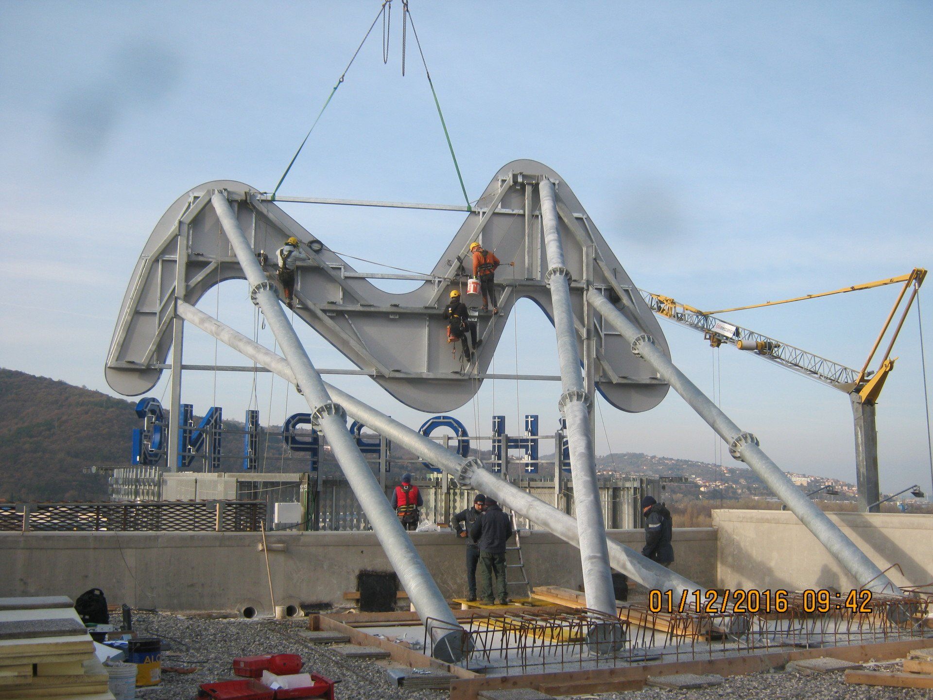 Operai che montano una grande struttura grigia ad arco con la scritta 